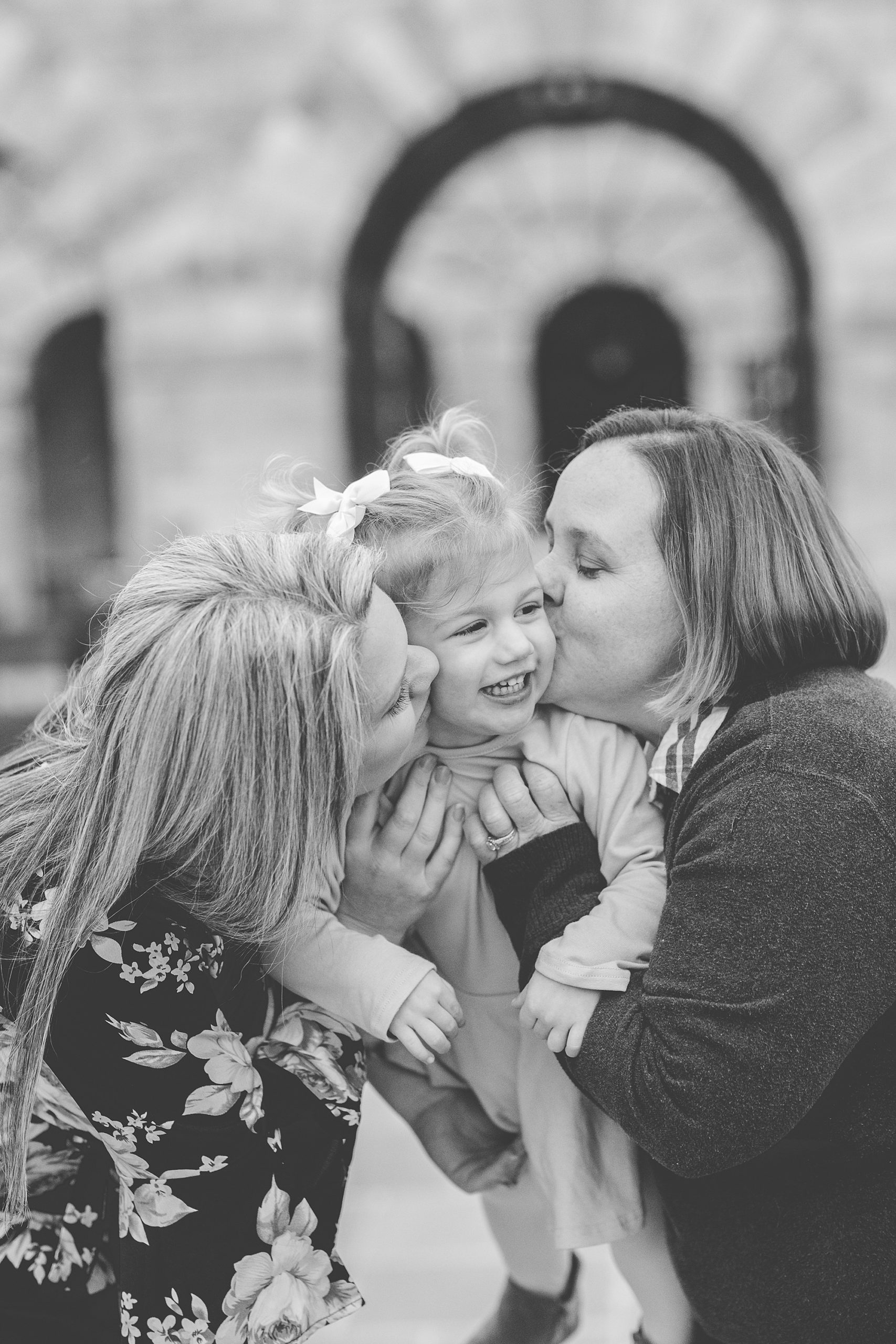 moms kiss daughter during maternity session at the Shrine of St. Anthony