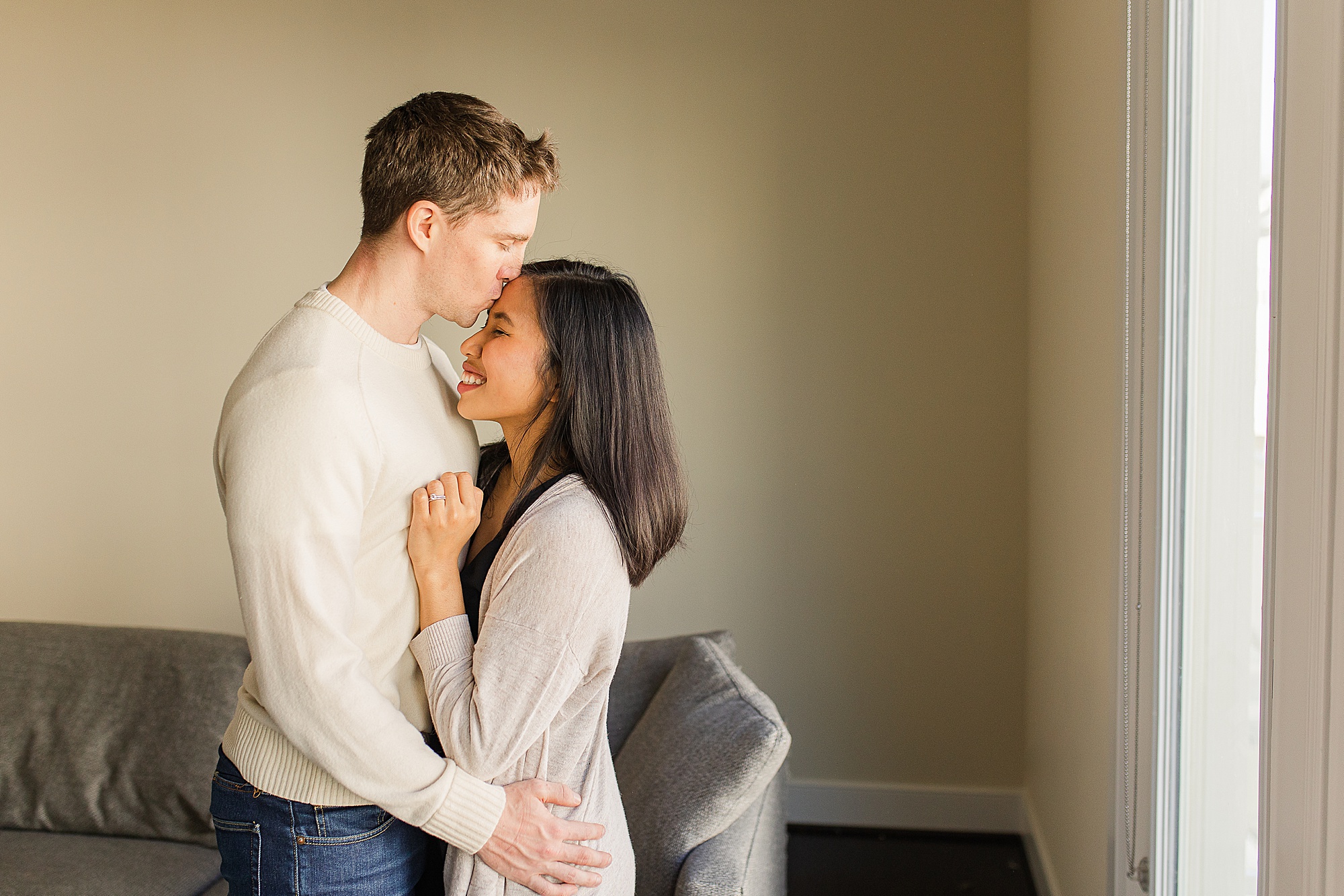 husband gives wife kiss on forehead during family photos at home