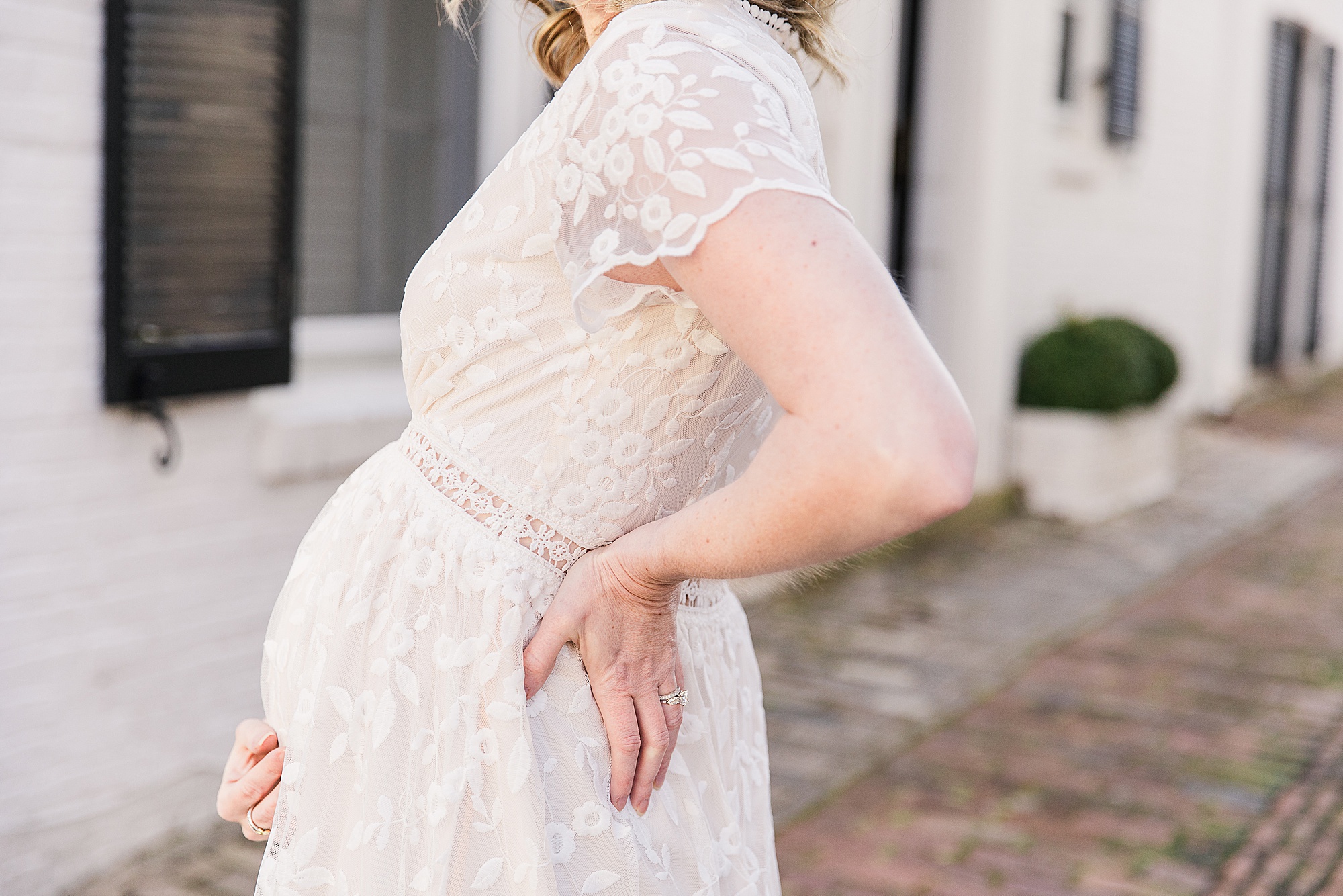 mom holds belly in white lace gown during maternity photos 