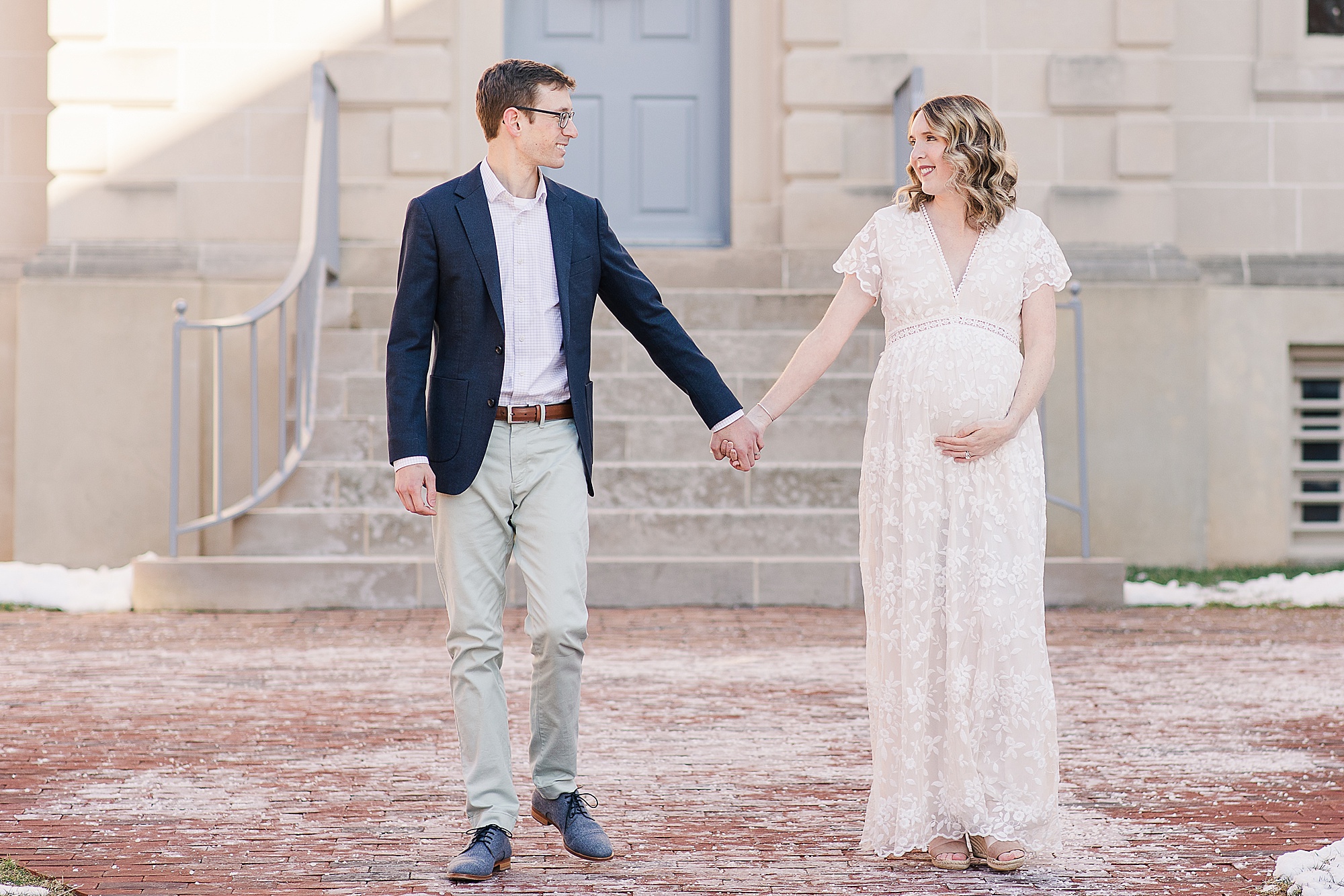 parents hold hands while mom holds belly during maternity photos
