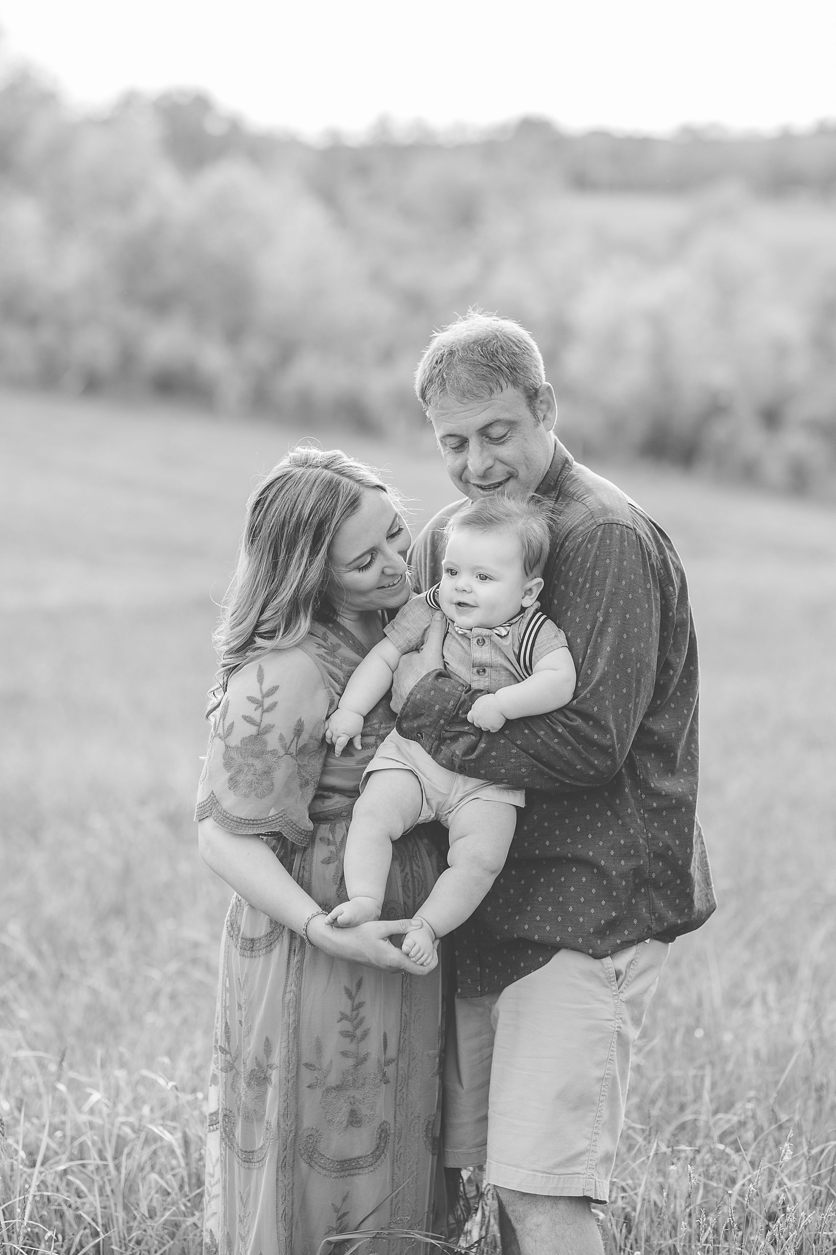 family of three poses in field together during family photos