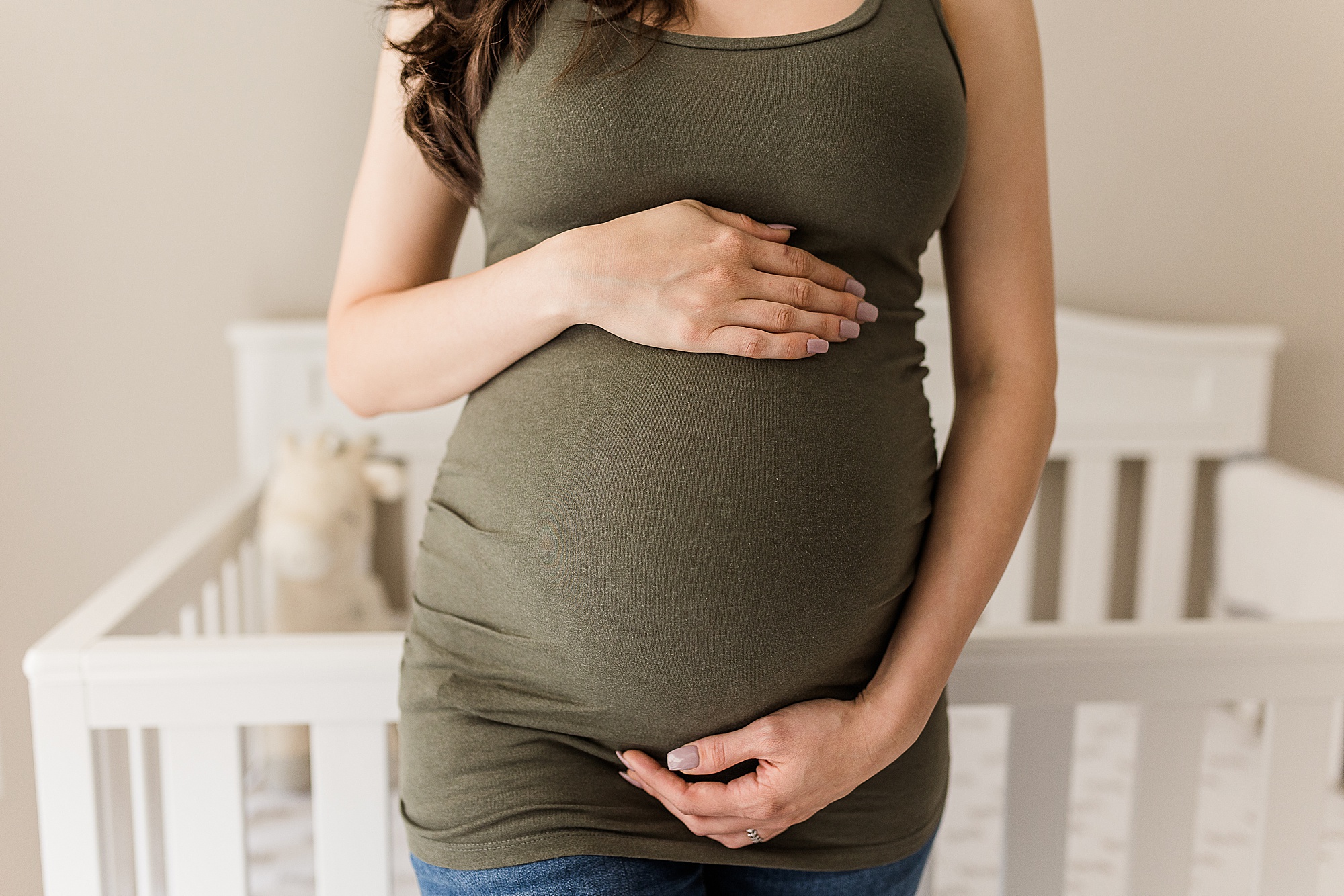 woman holds belly standing by crib