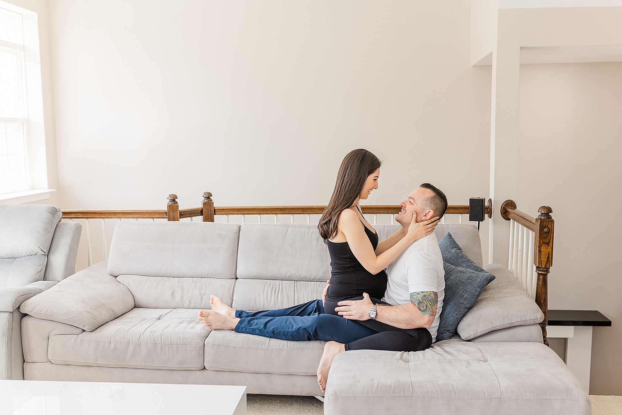 couple sits on couch at home during maternity photos