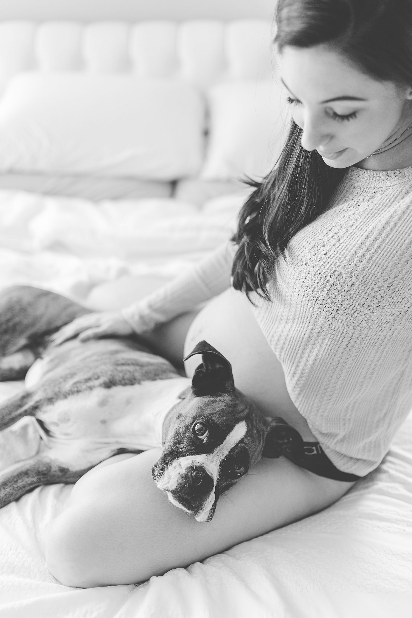 woman sits with dog in lap during at-home maternity session