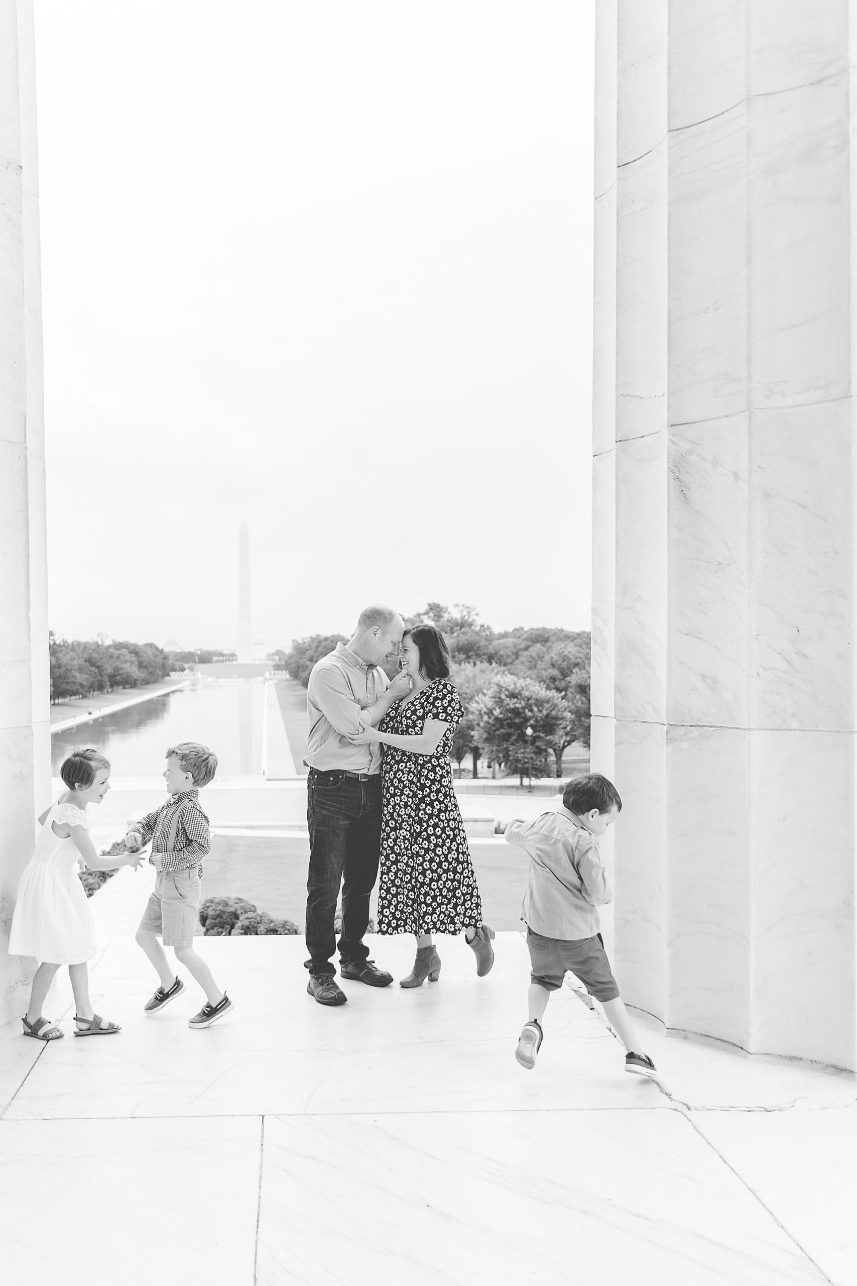 parents smile together while kids run around during Washington DC Family Portraits