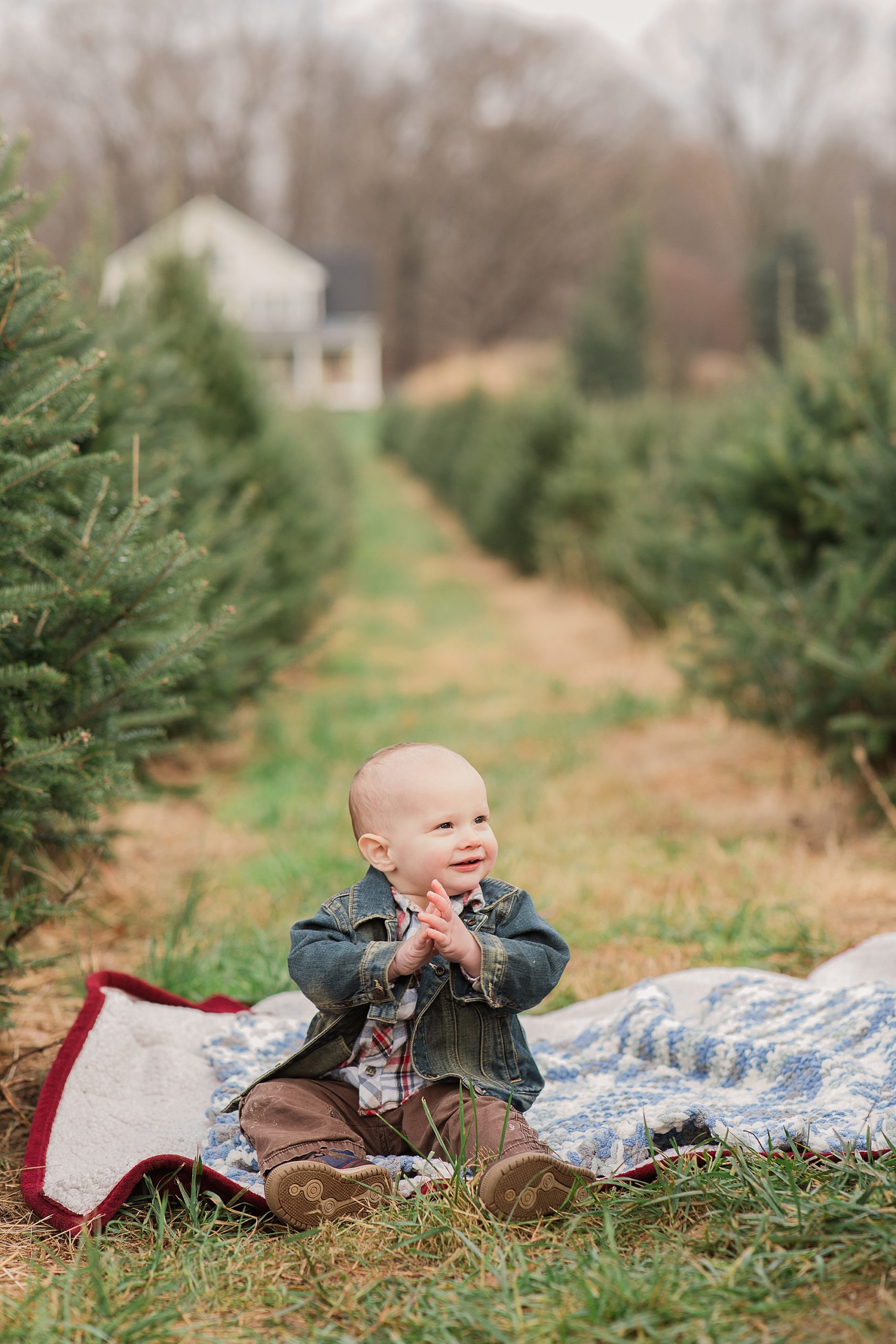 baby sits on blanket among trees at Greenway Tree Farm