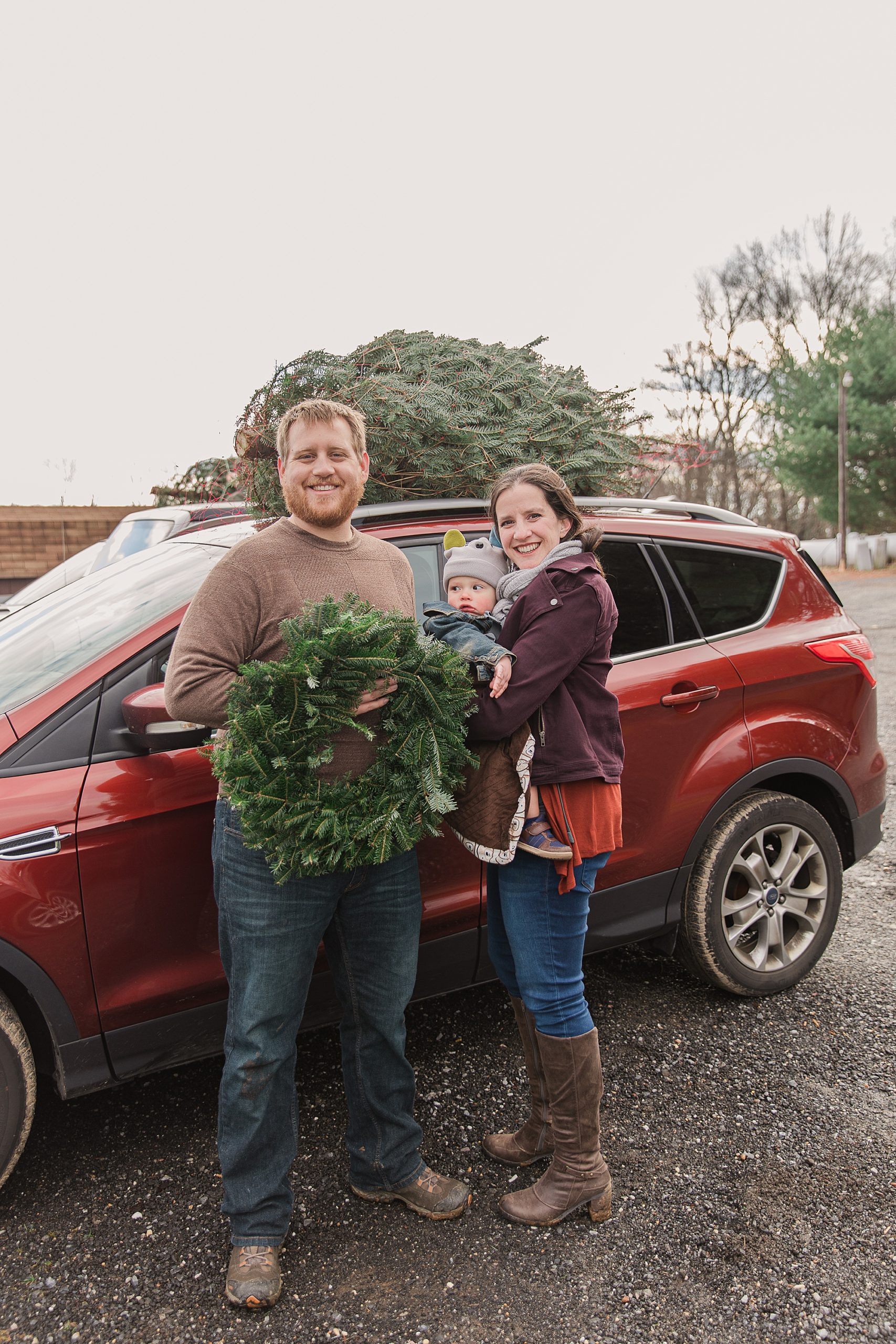 family poses by car with Christmas tree during Greenway Tree Farm lifestyle family portraits