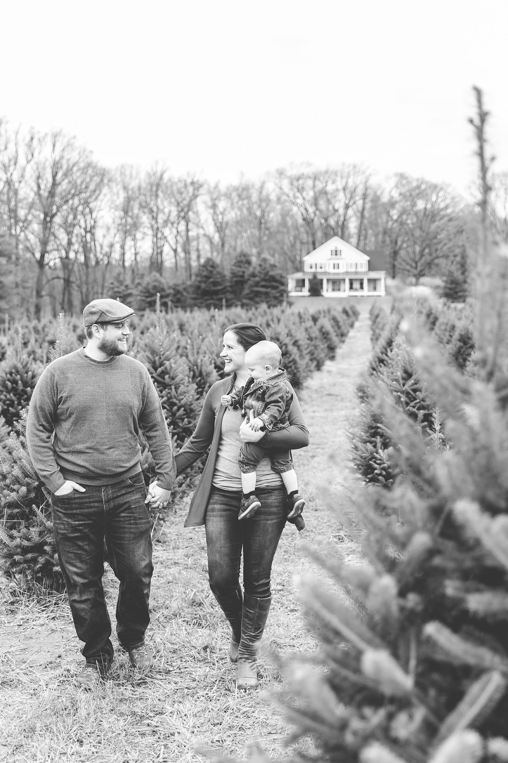 family of three walks down row of Christmas trees
