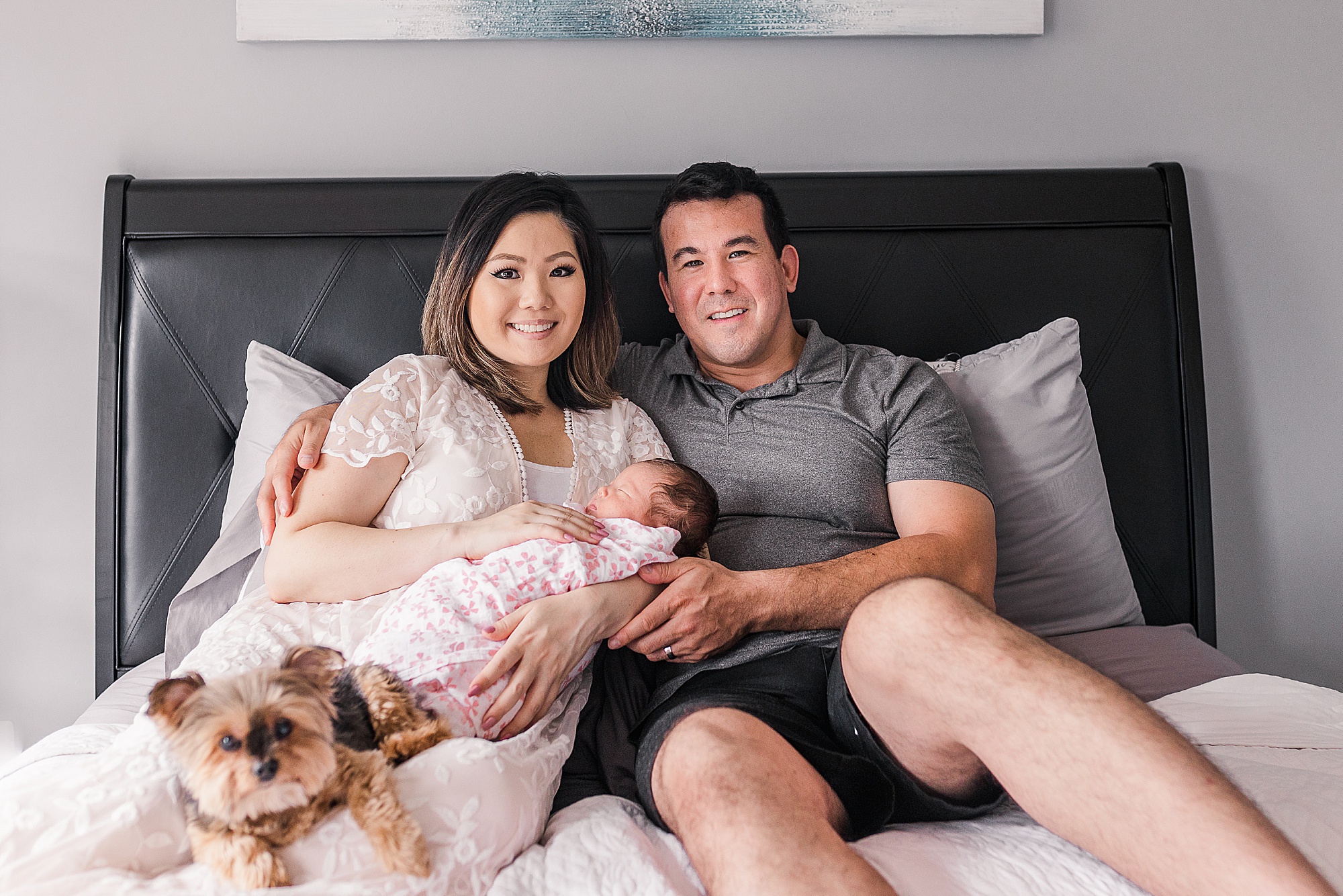 couple sits on bed with new baby girl and dog during lifestyle newborn portraits at home