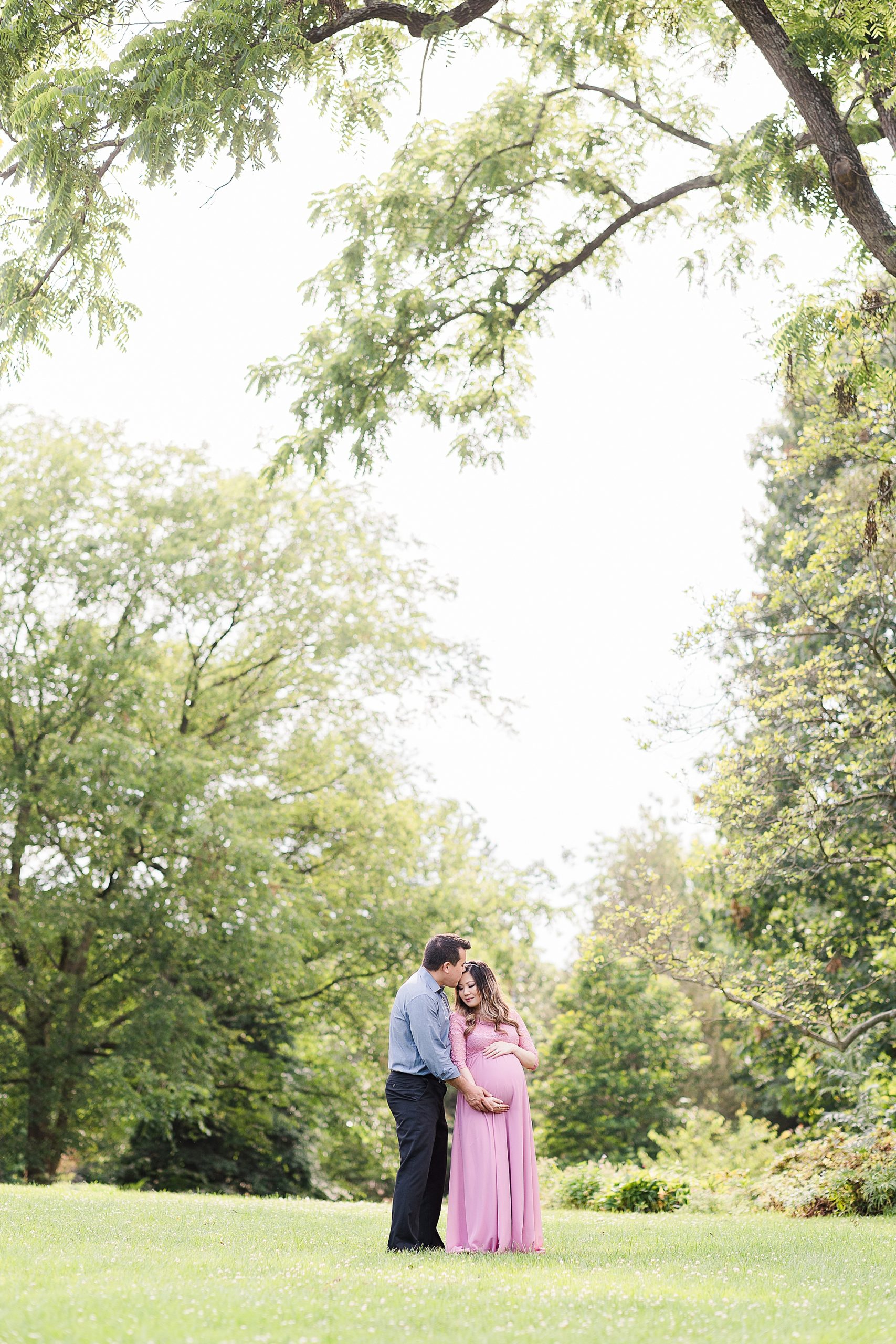 couple stands under trees during Alexandria VA maternity portraits 