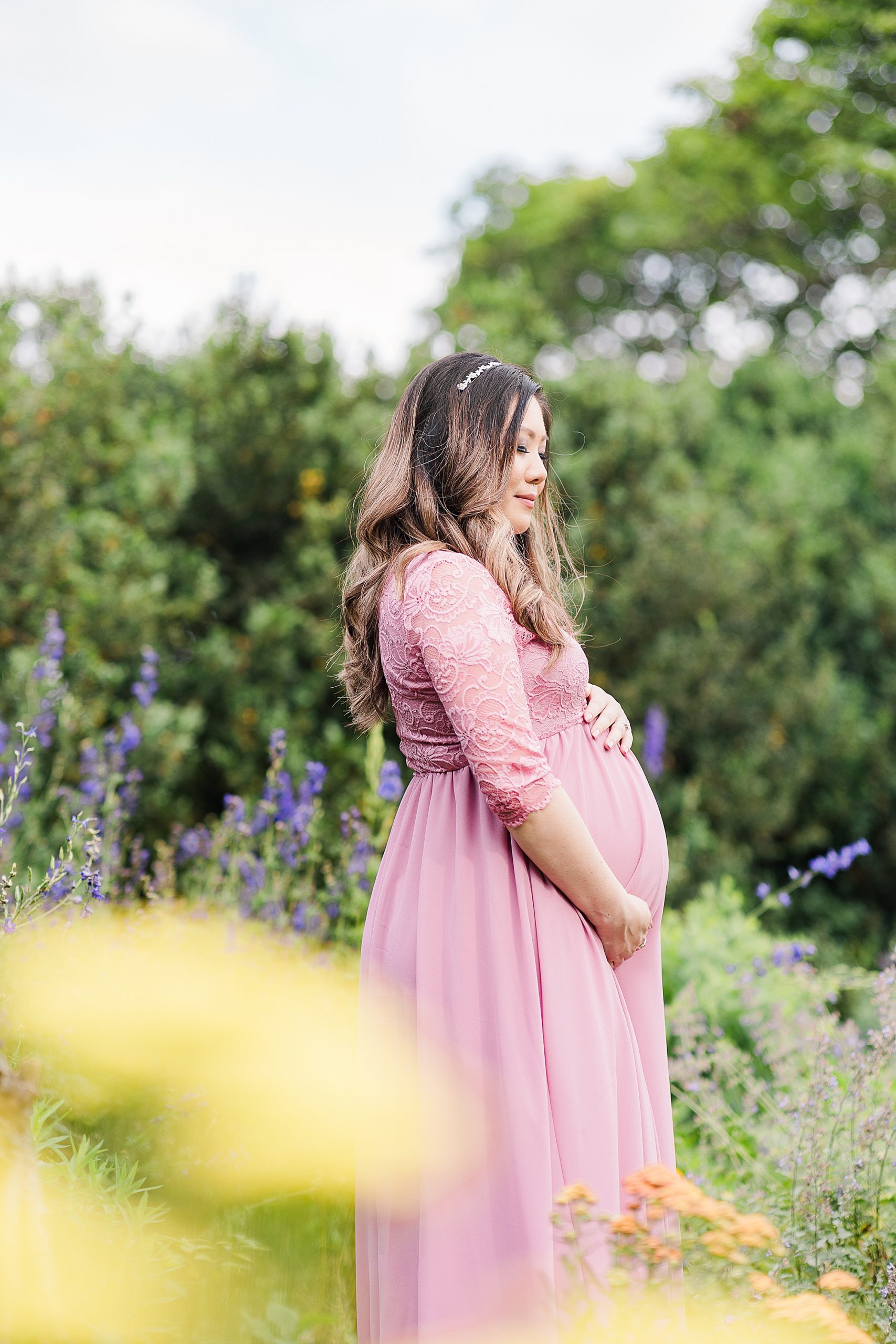 woman stands in gardens holding belly in pink gown