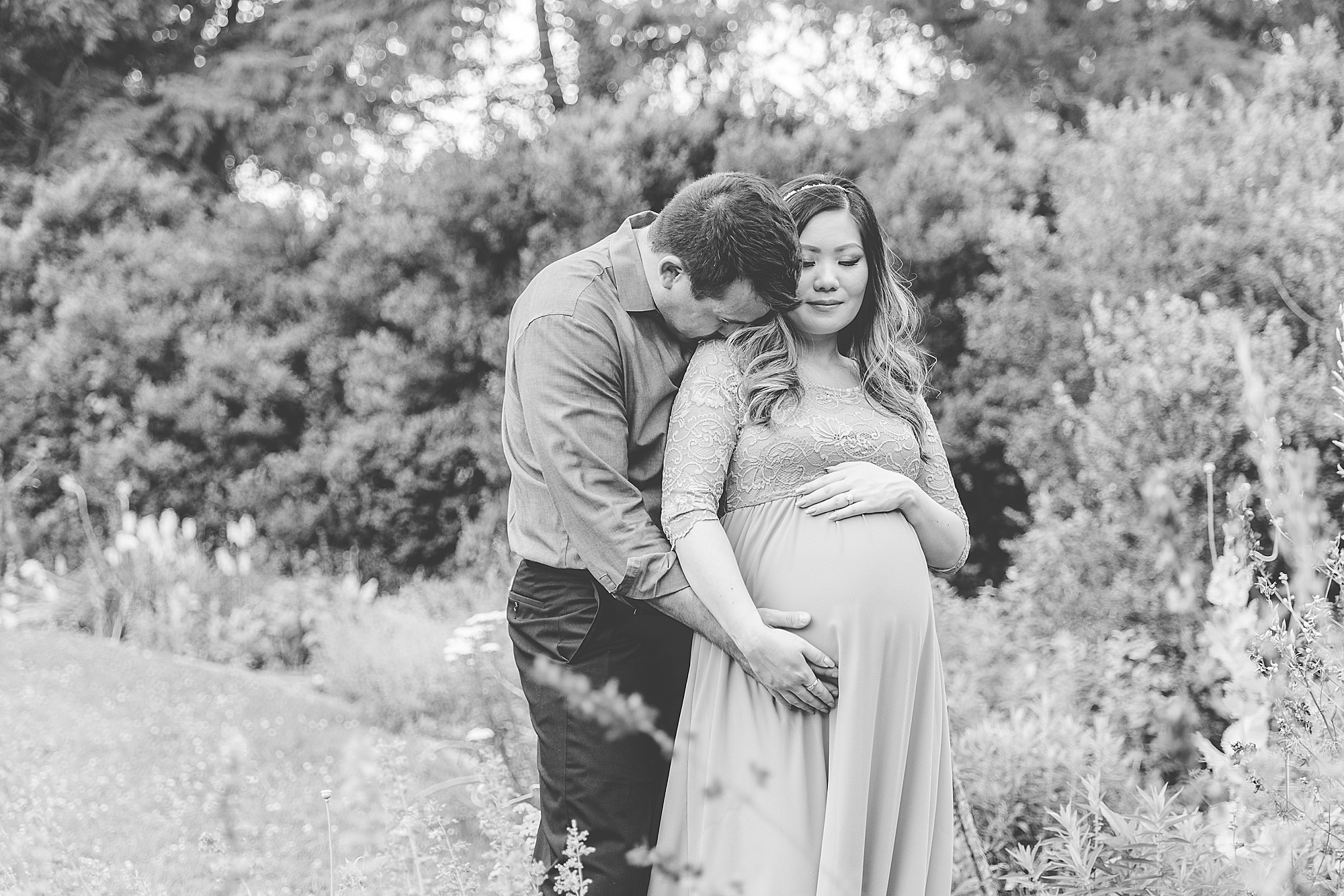 man kisses wife's shoulder during Green Spring Gardens maternity session