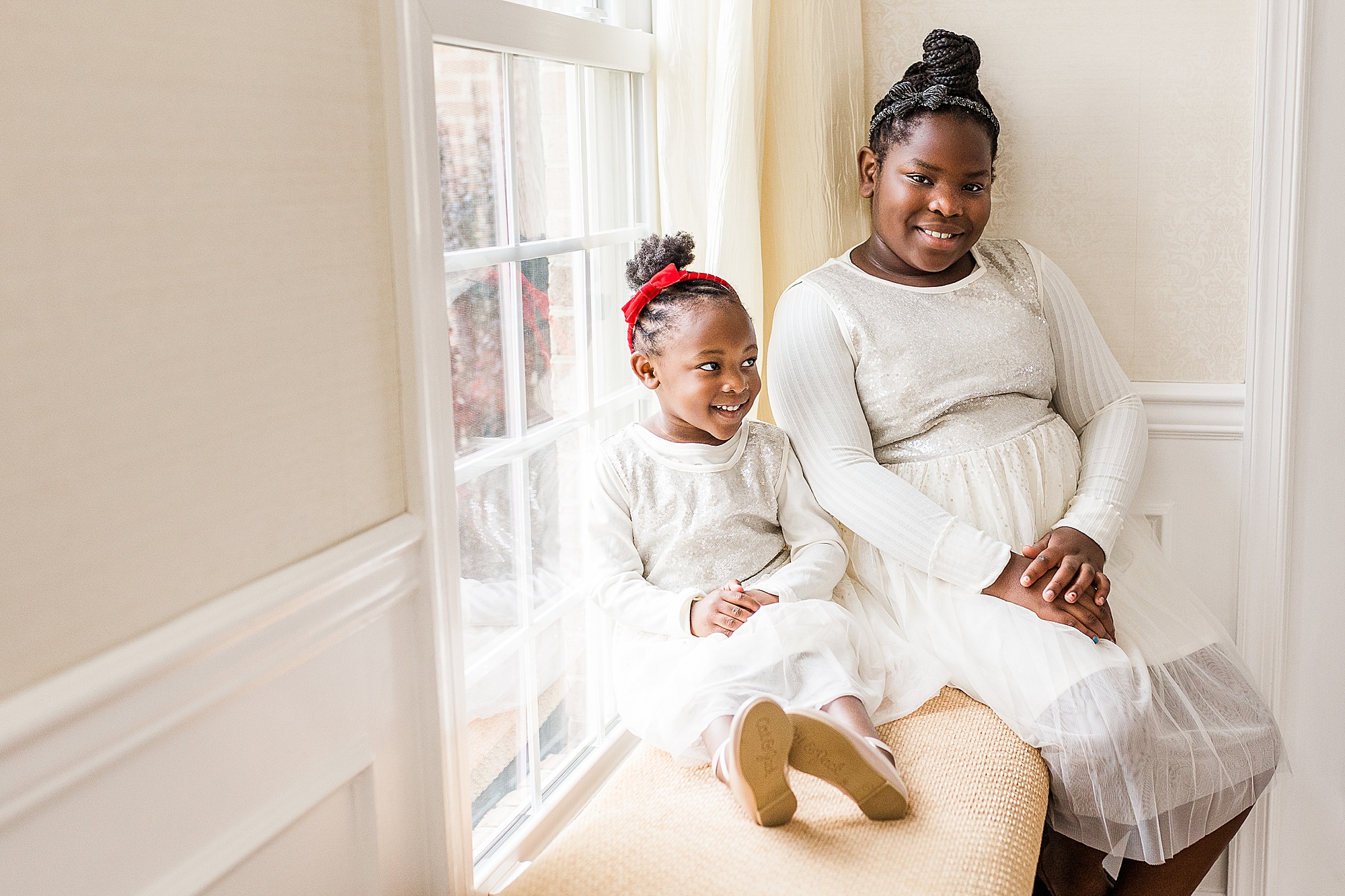sisters sit in window seat during Howard County In-Home Holiday Family Session