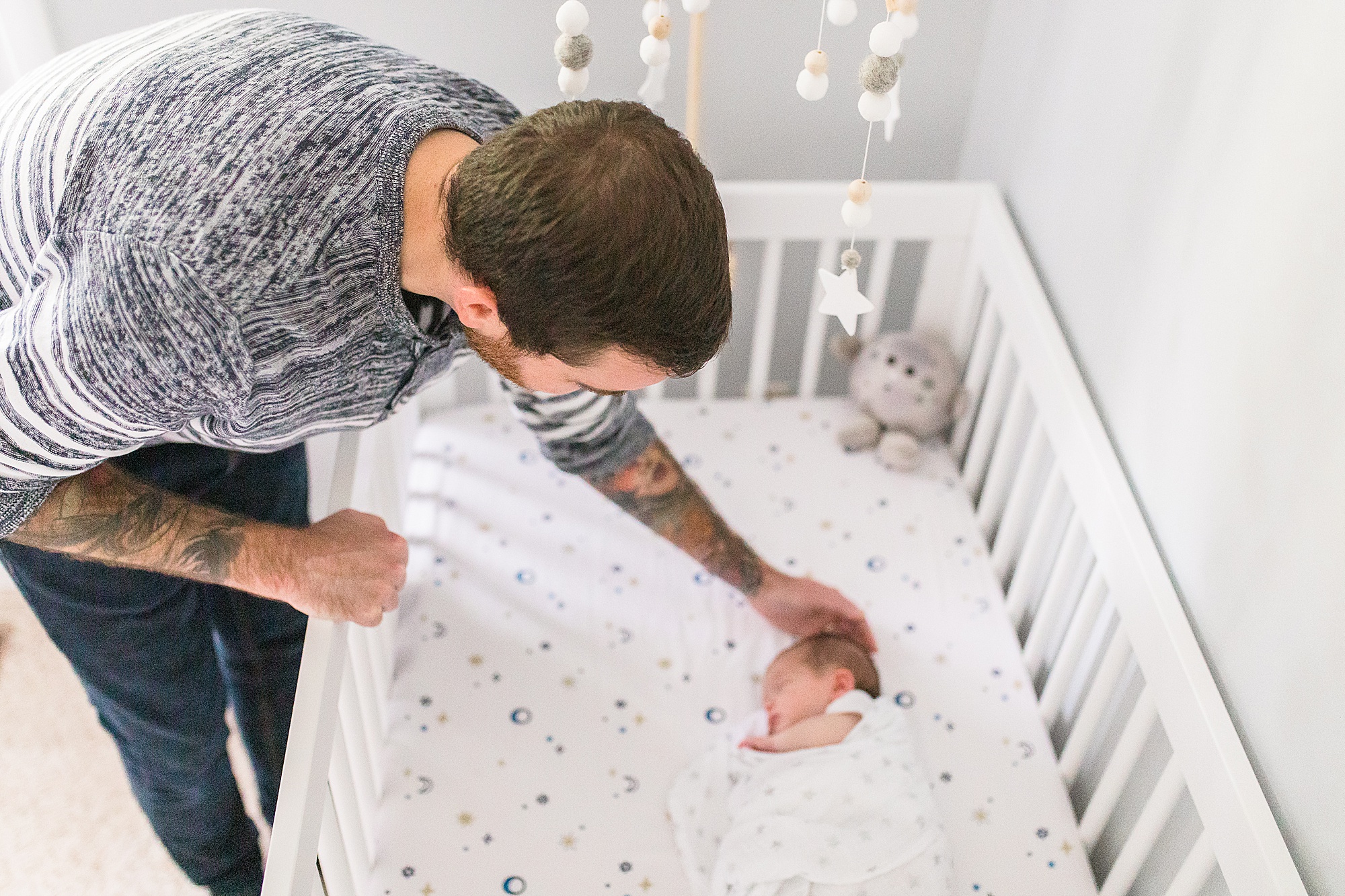 dad leans over crib railing to touch son during Annapolis lifestyle newborn session