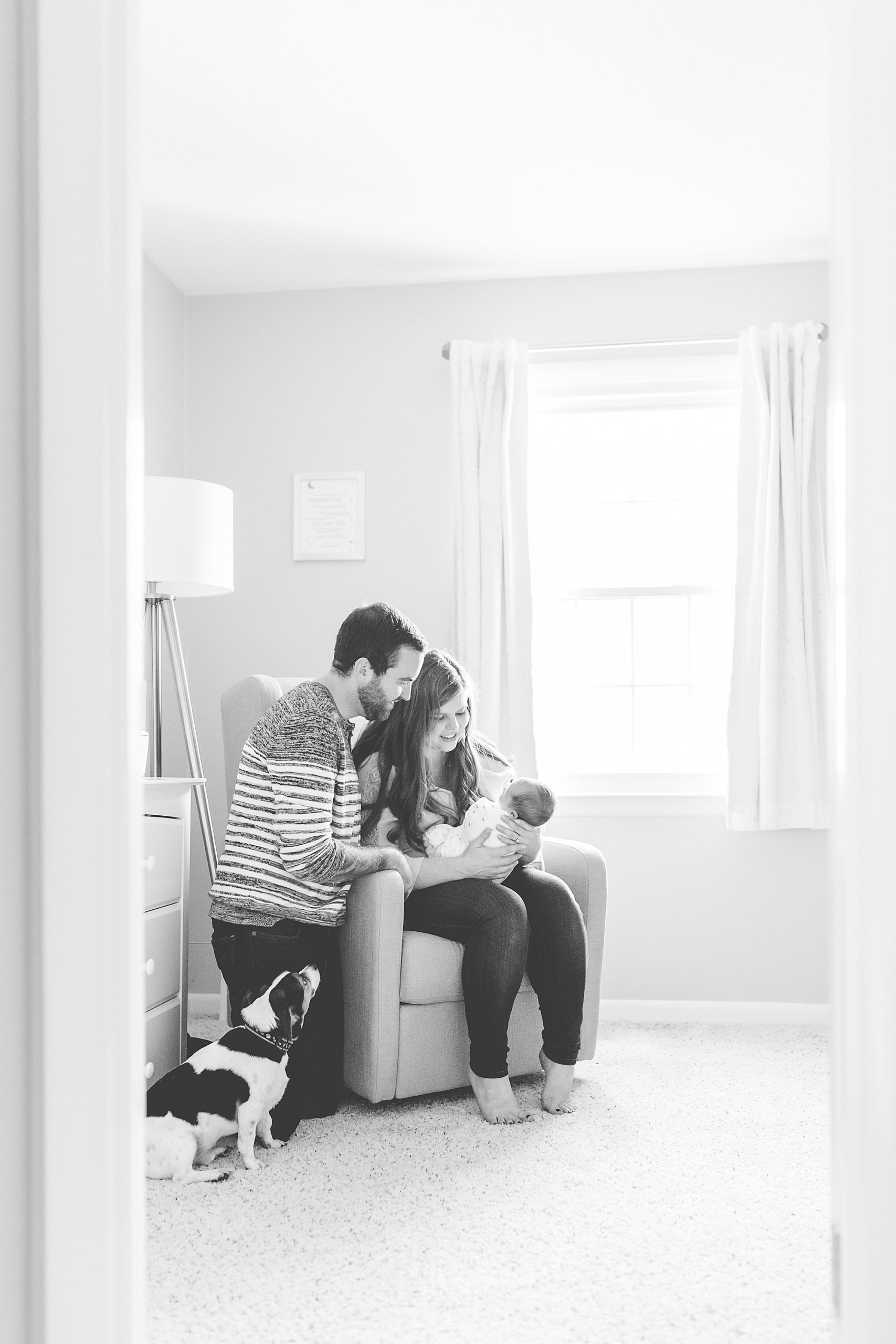 parents hold baby boy sitting in corner of nursery