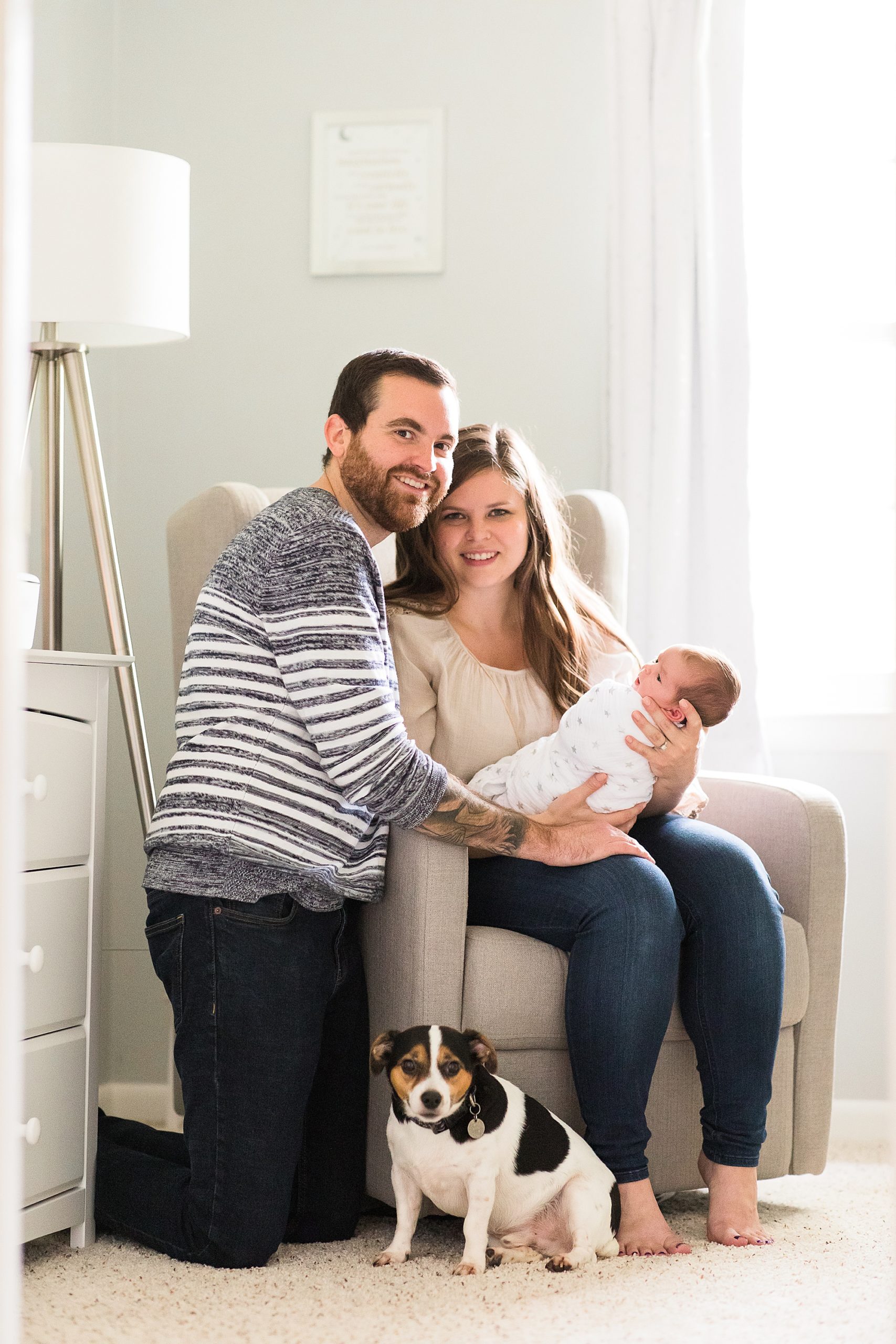 parents sit with baby and dog during newborn portraits at home