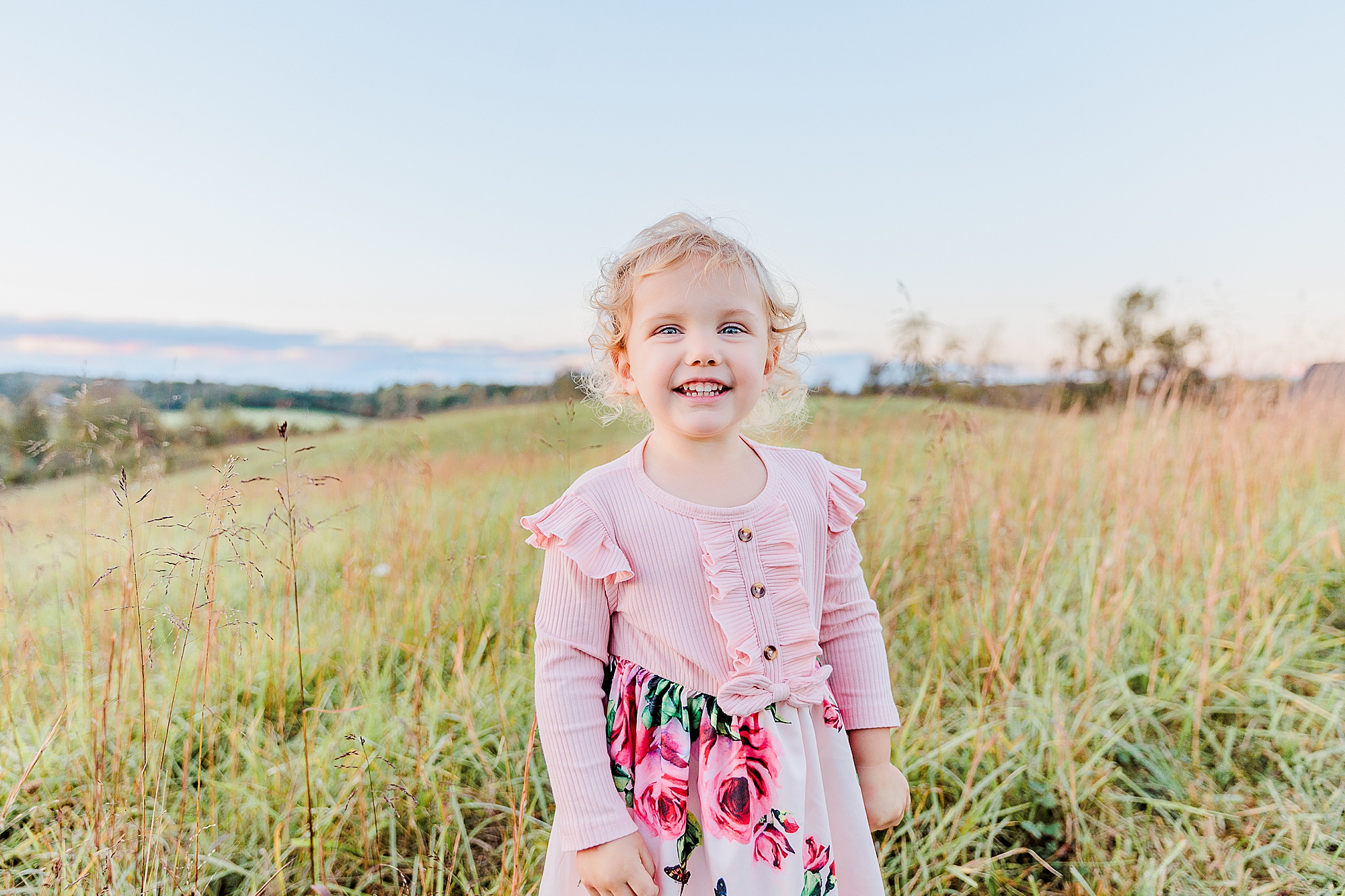 little girl in pink dress smiles in field during fall photos