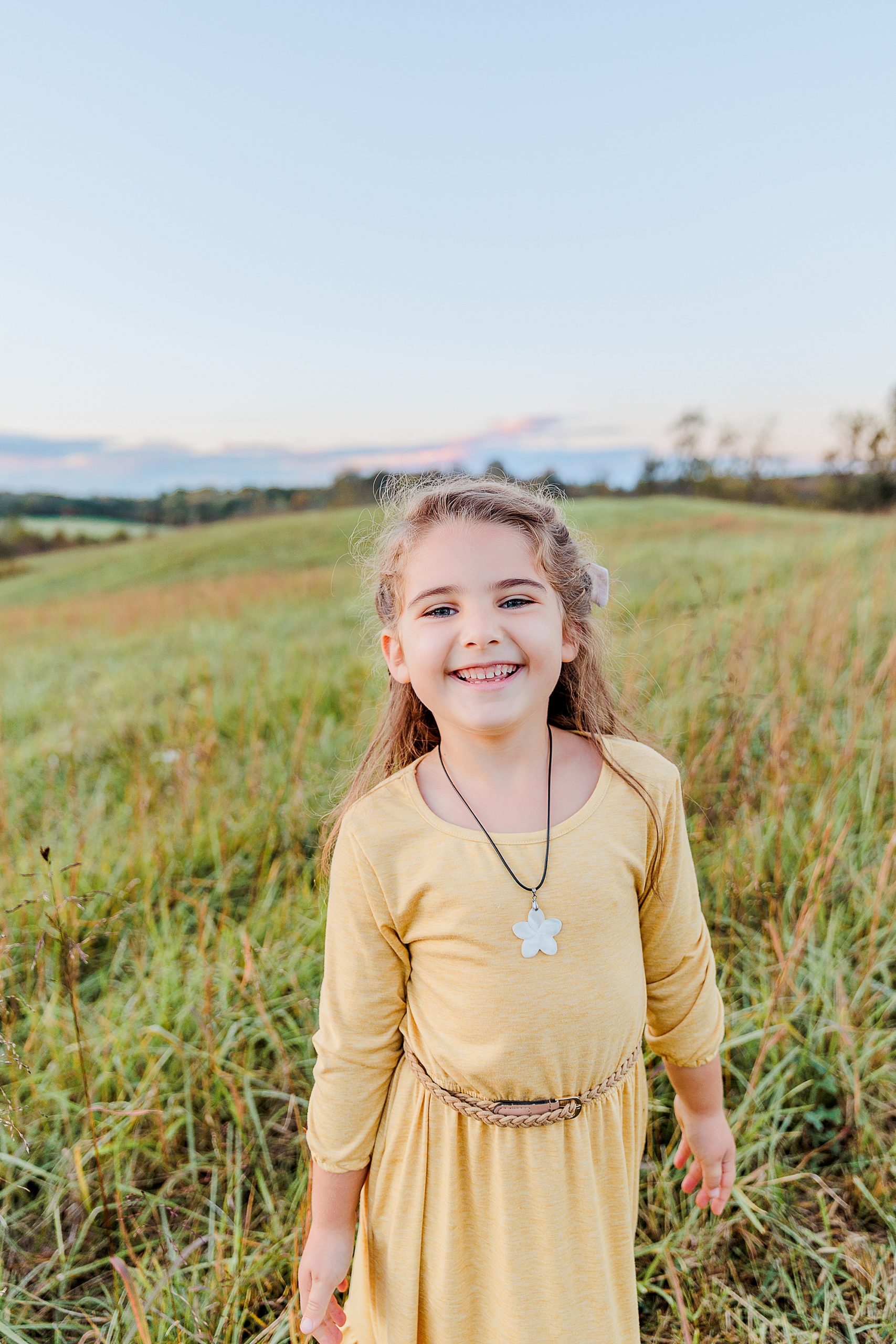 young girl in yellow dress smiles standing in field