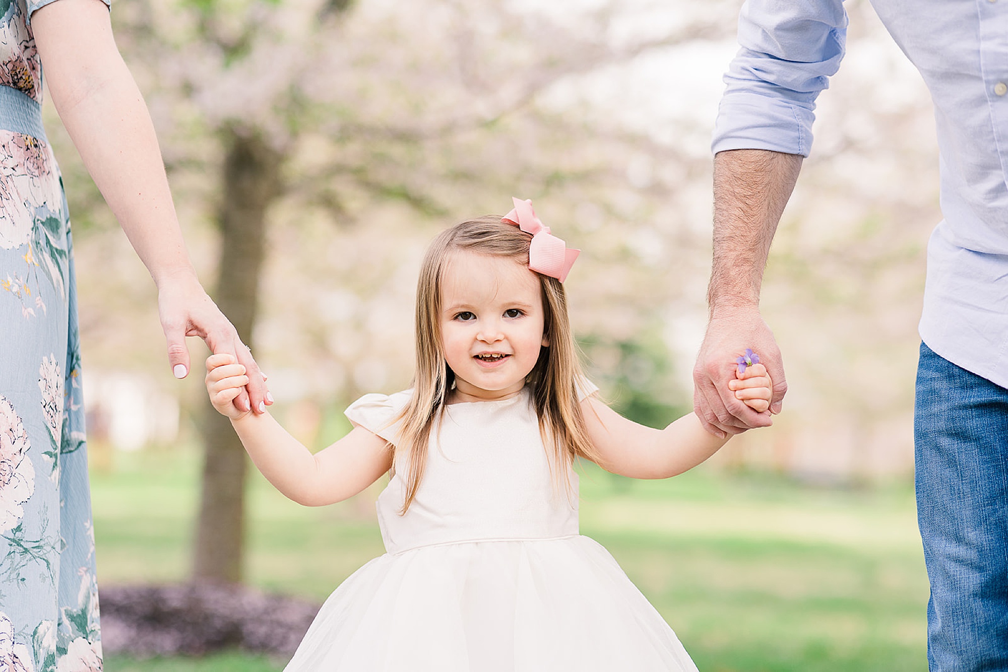 parents hold daughter's hands during spring photos in Ellicott City MD