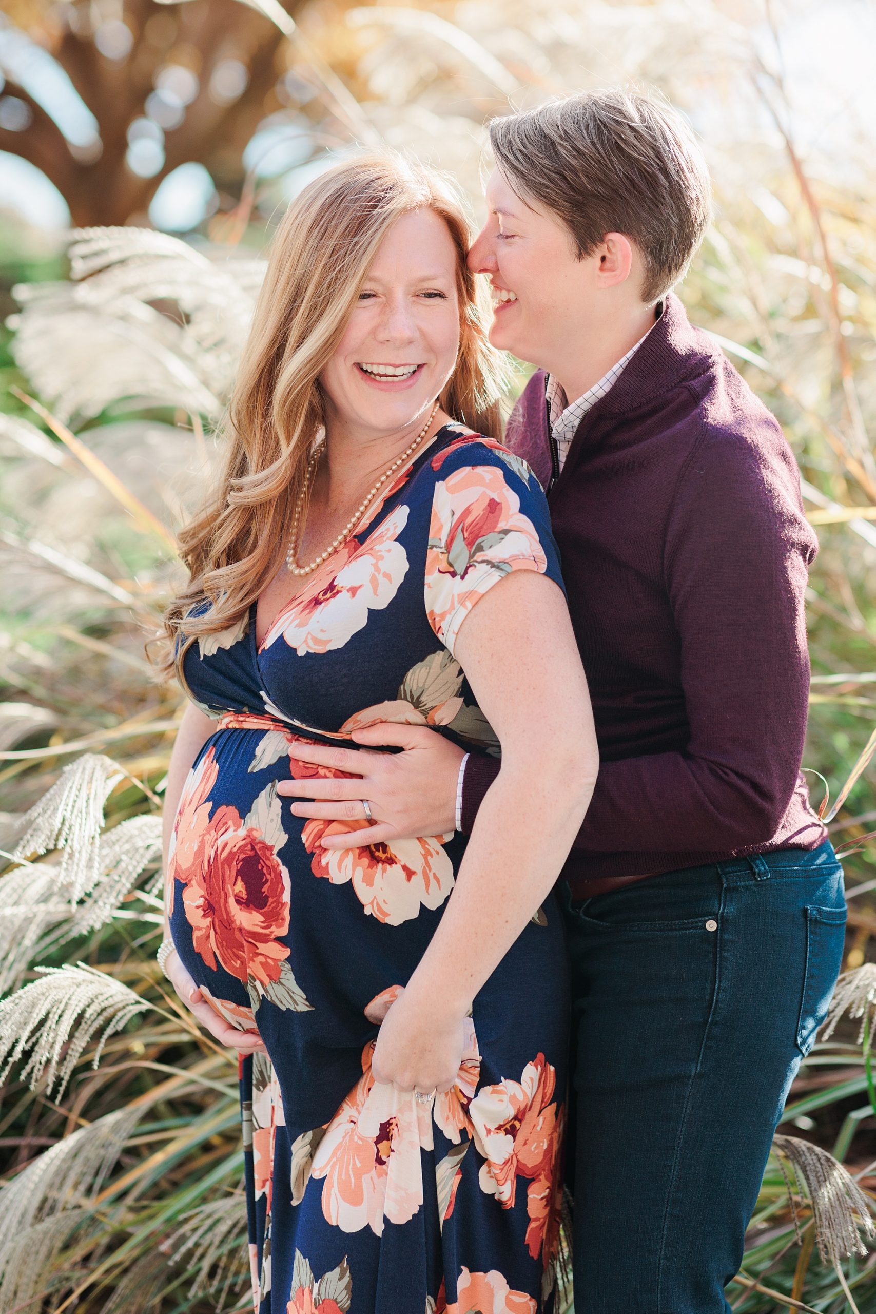 woman laughs with same-sex partner during fall maternity portraits in Ellicott City