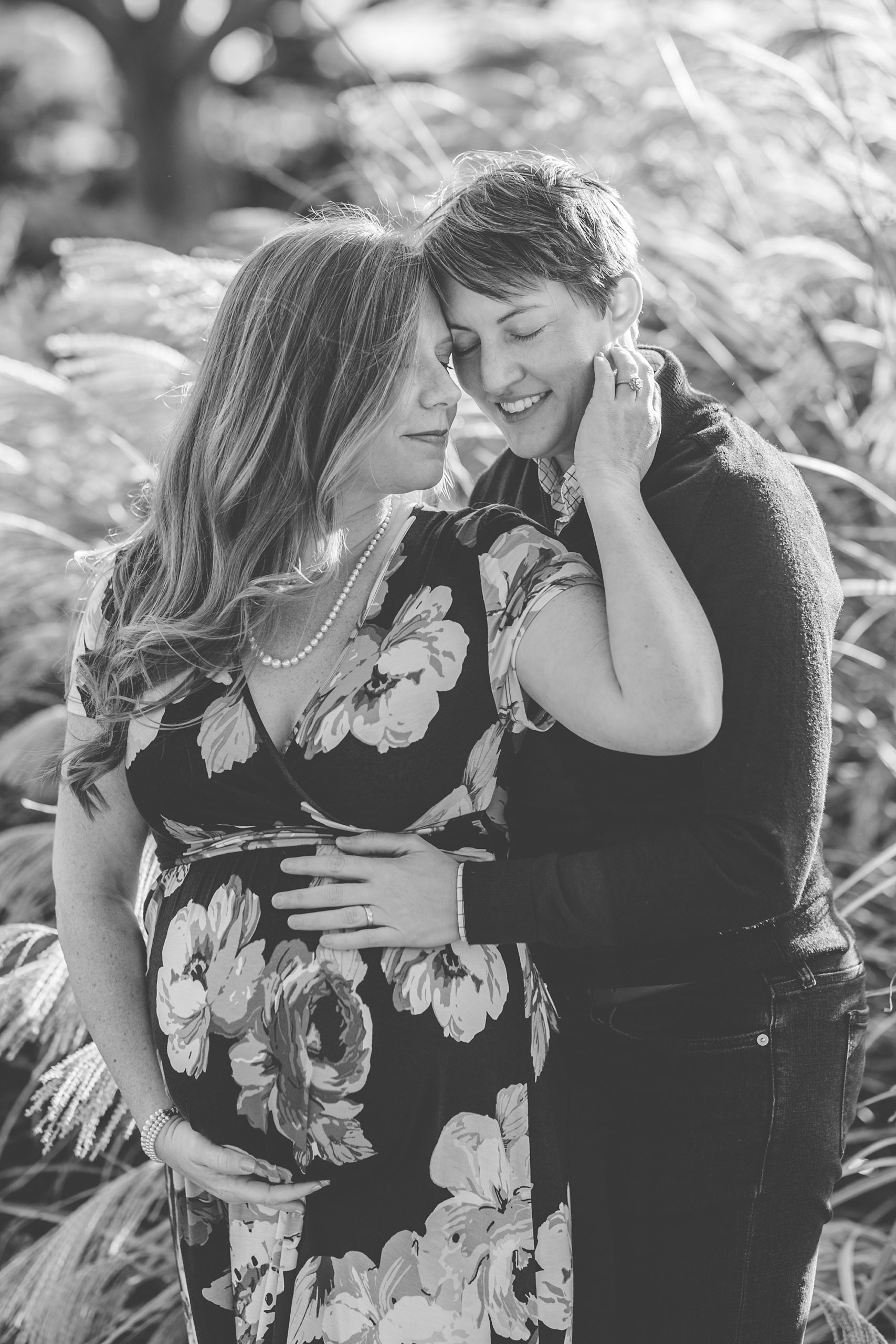 two women pose together in tall grass during fall maternity portraits