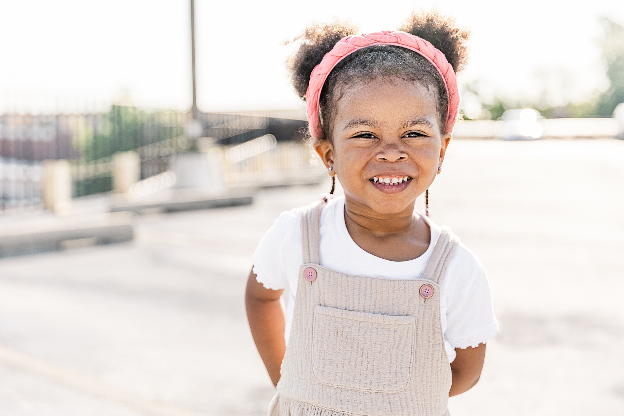 little girl in overalls smiles with pink headband during Annapolis family portraits