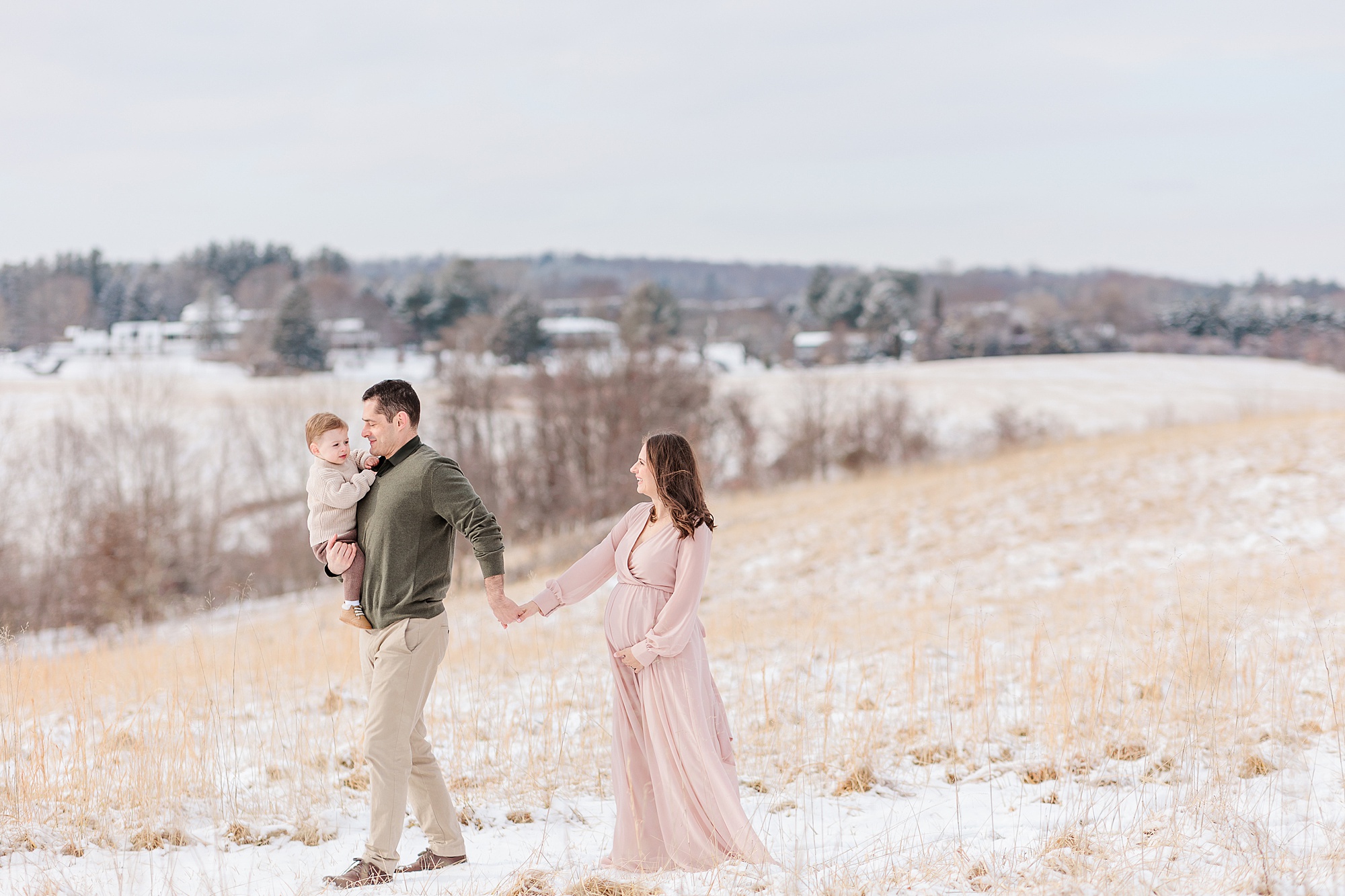 family walks along hill during snowy maternity session