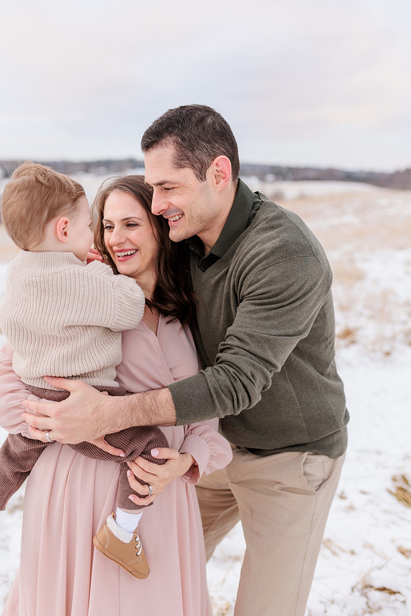 couple laughs with son during maternity photos in the snow