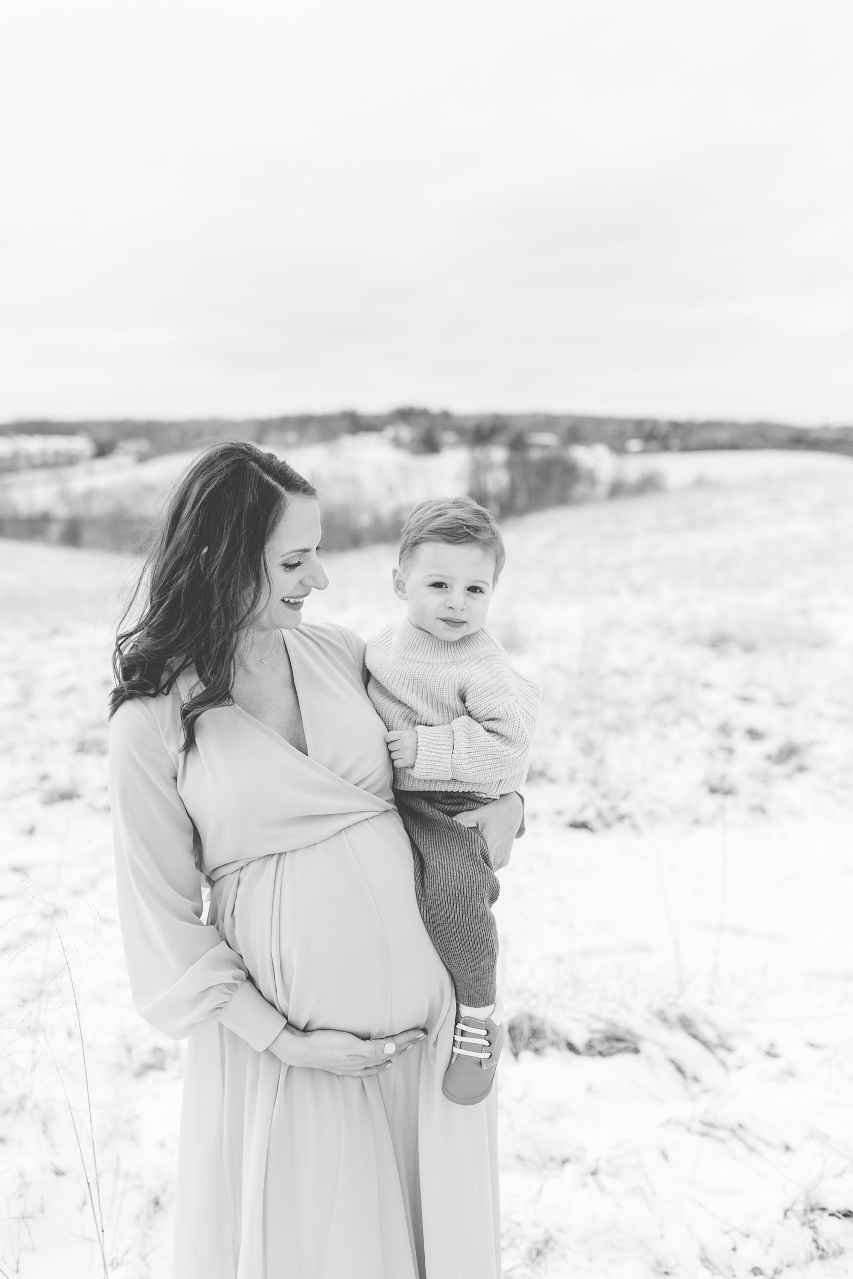 mom holds son and belly during snowy maternity session