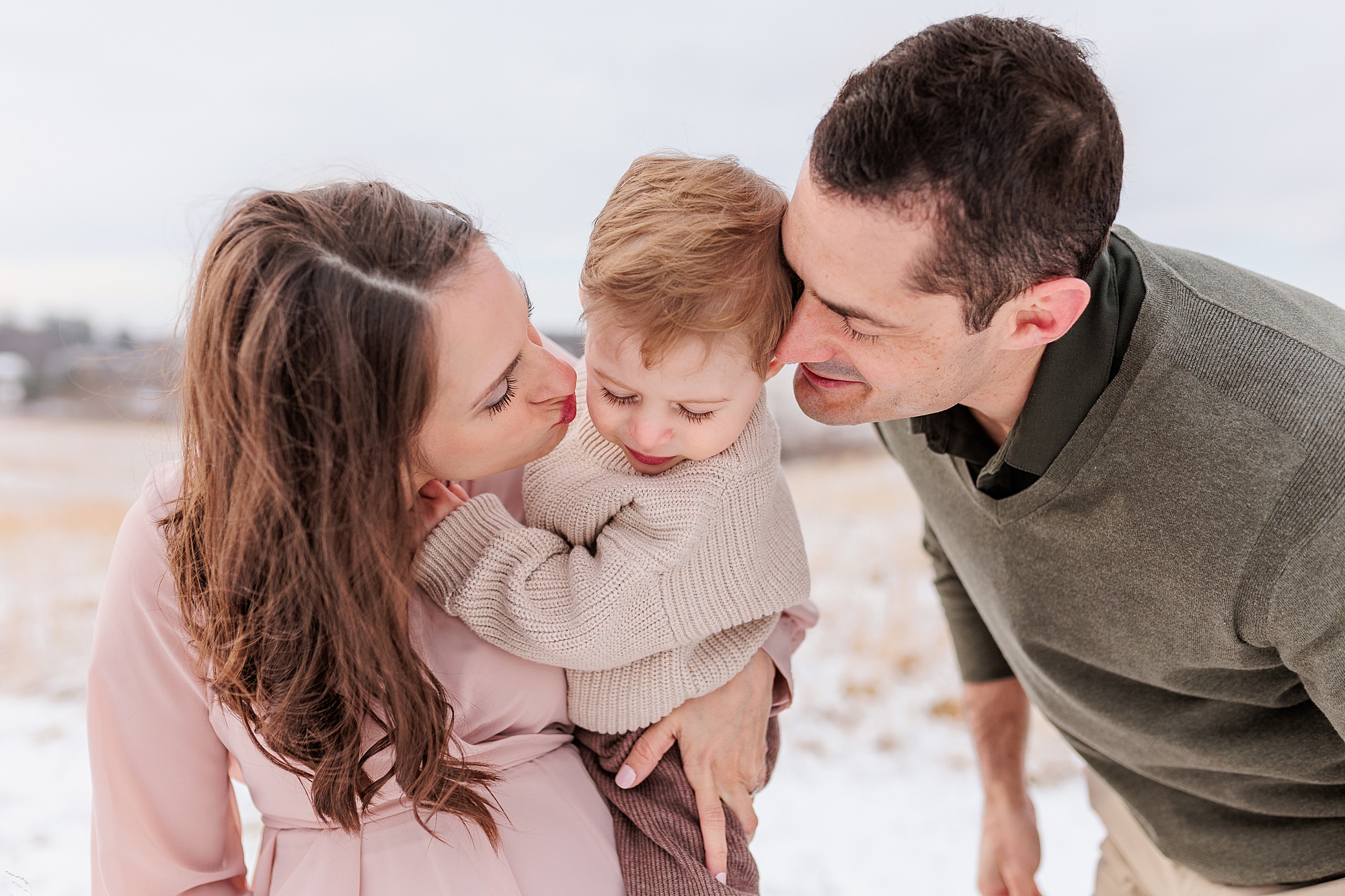 parents play with toddler during maternity photos in the snow