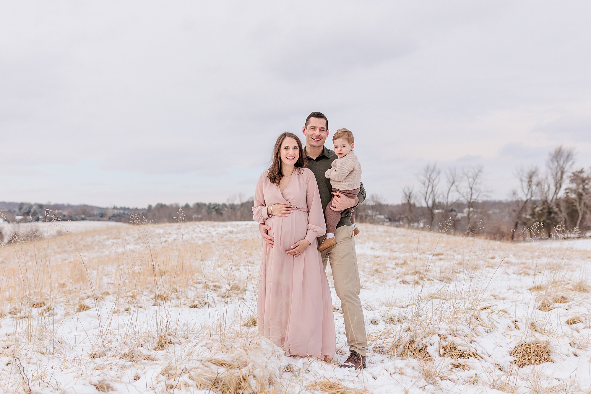 family of three poses on hill in Howard County during snowy maternity session