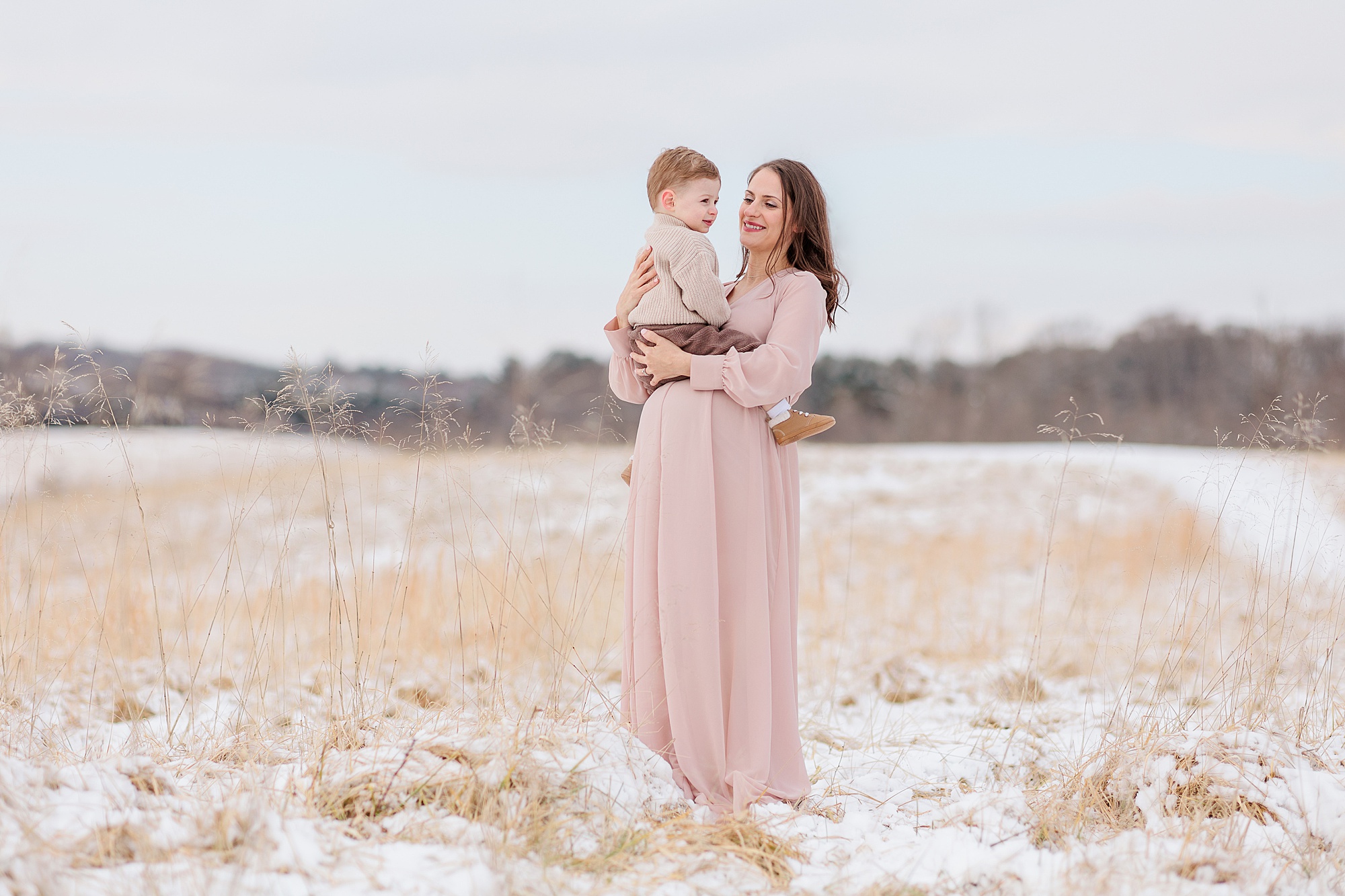 woman and son pose in the snow during maternity photos 