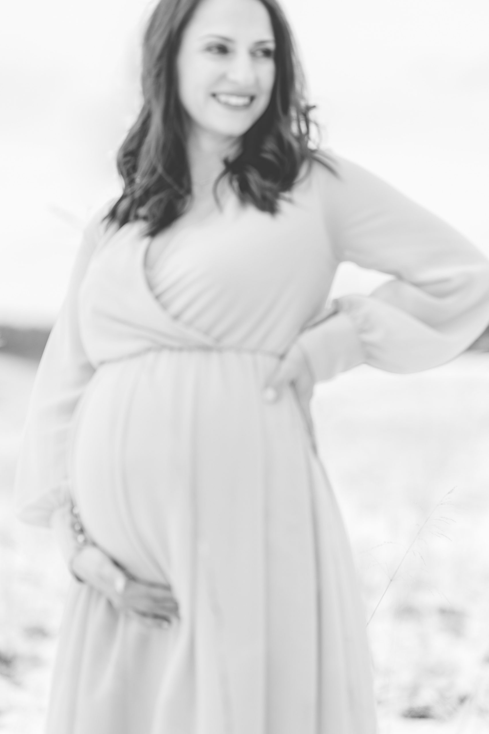 expecting mother poses holding back and baby belly during snowy maternity session