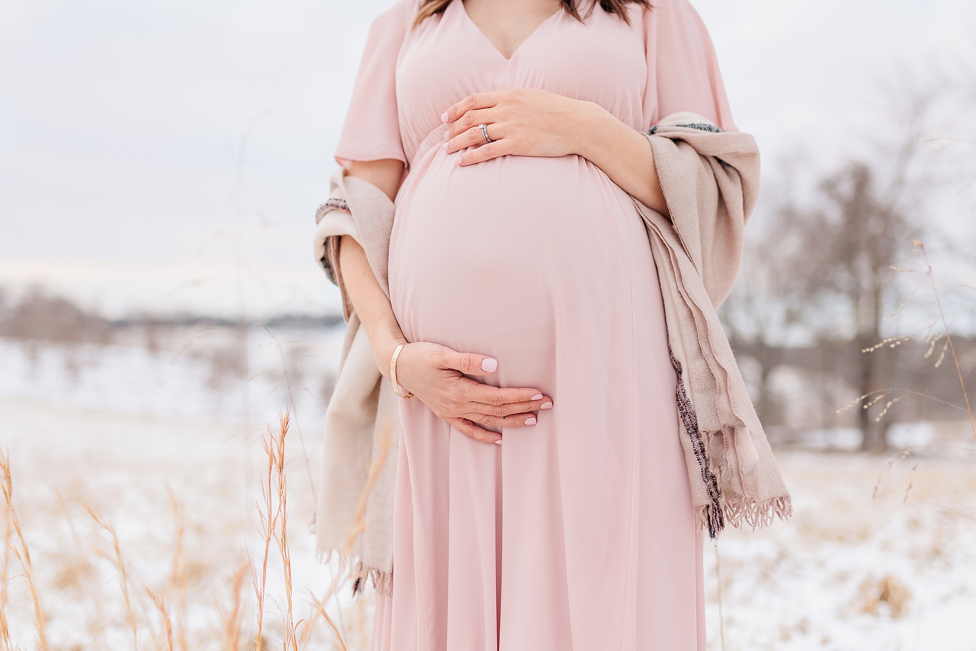 mom in pink gown holds belly during snowy maternity session