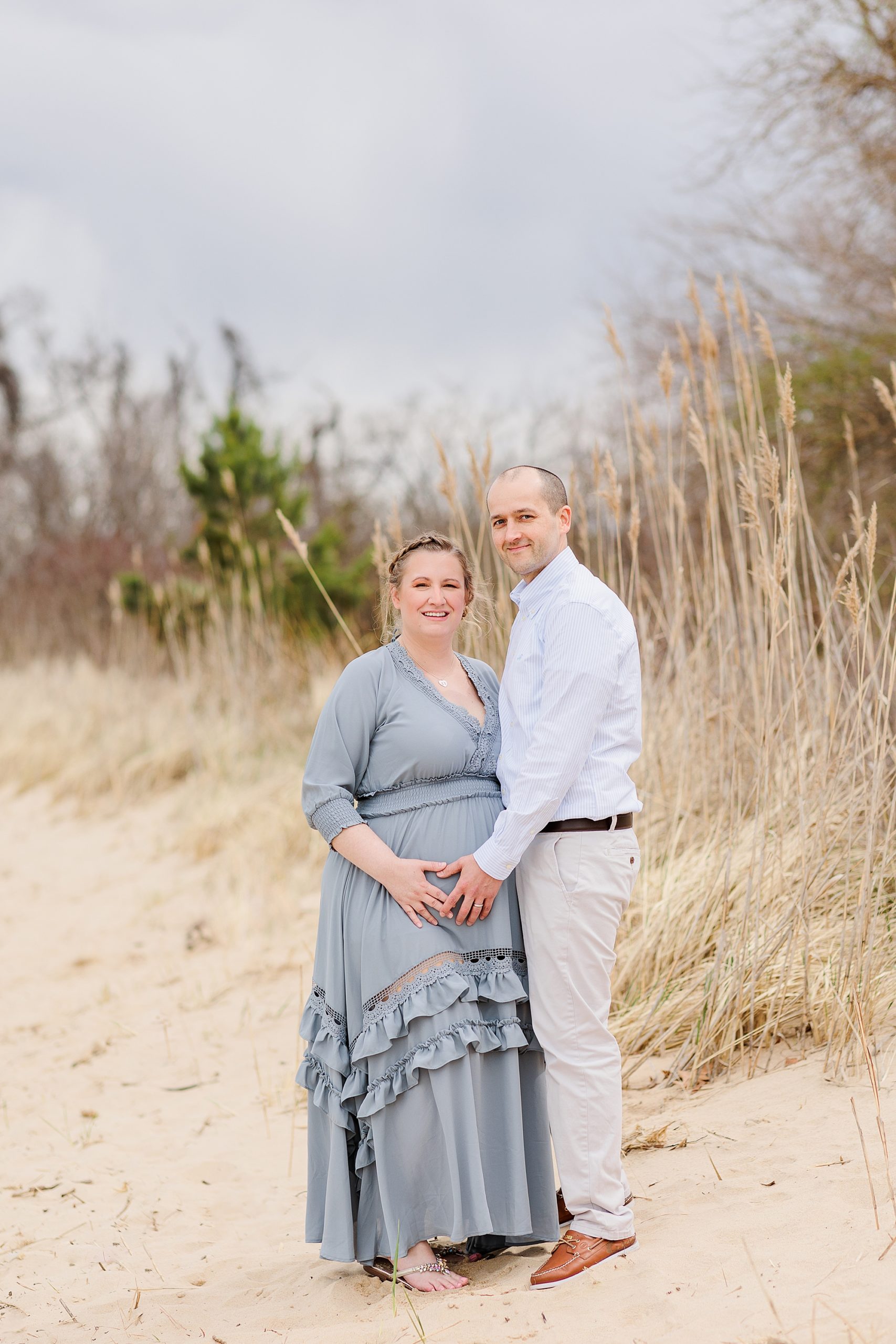 woman in flowing maternity dress stands on beach with husband