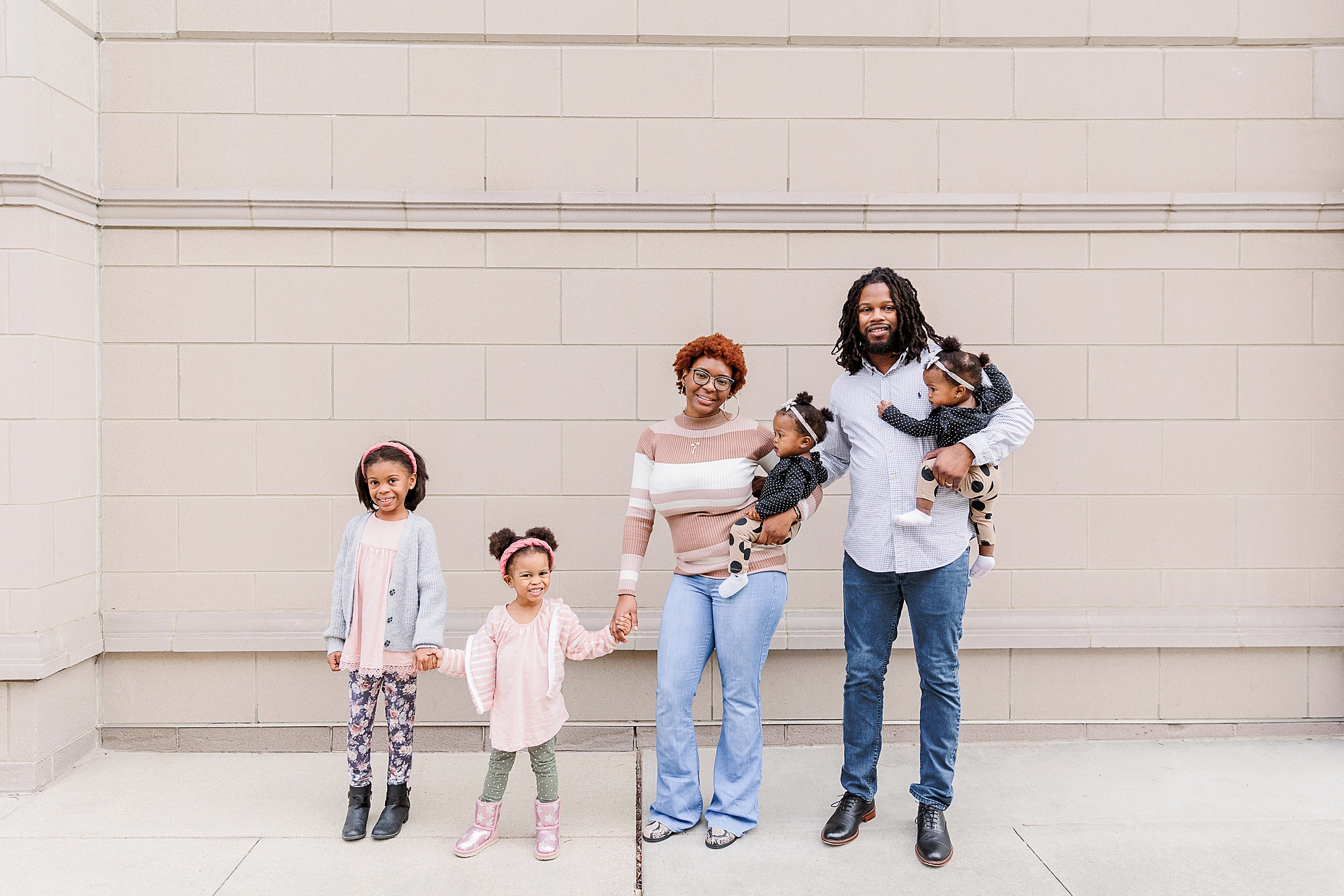 family of six holds hands standing against white wall during Annapolis family portraits