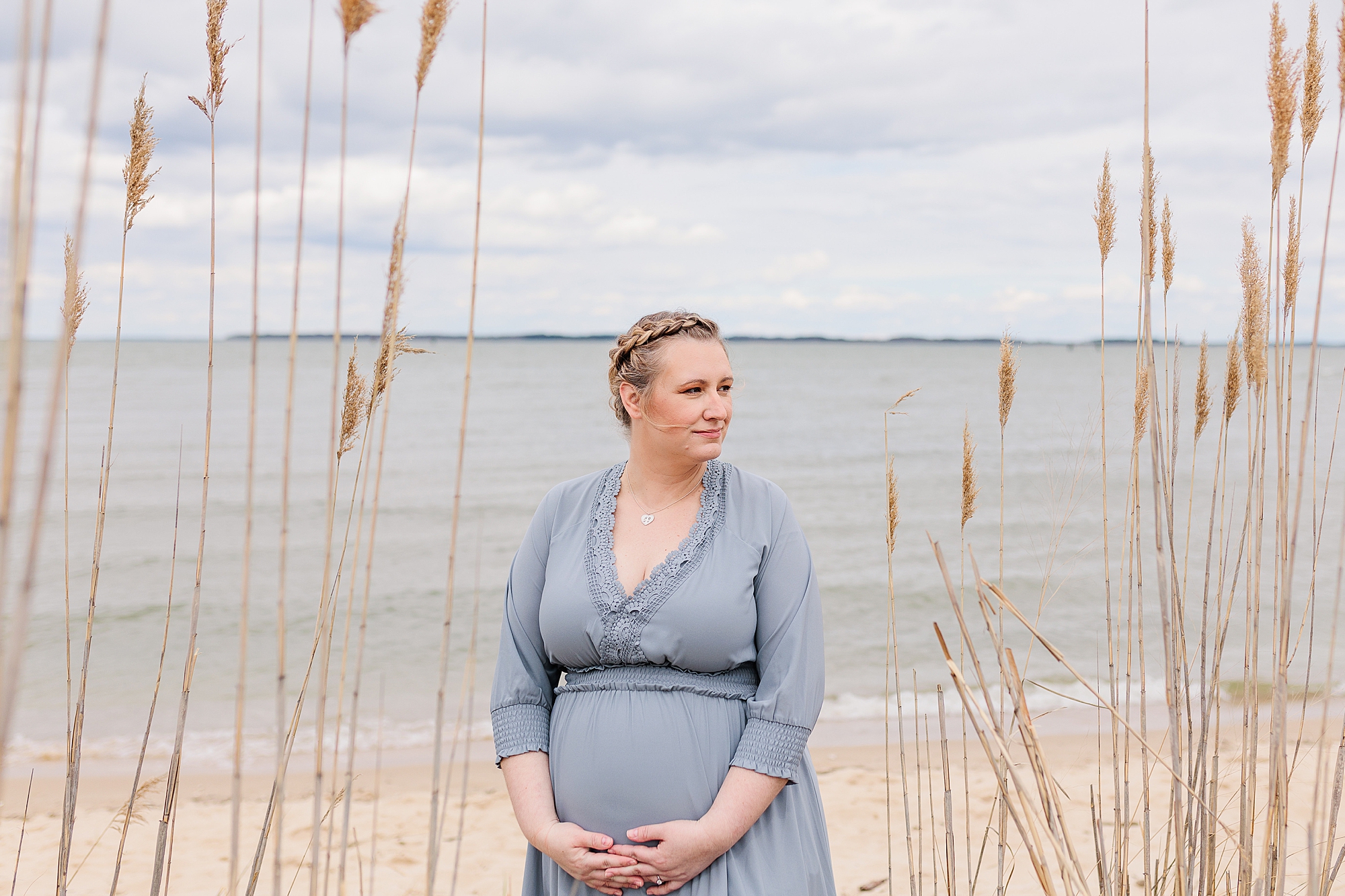 mom stands holding baby bump during maternity photos on the beach
