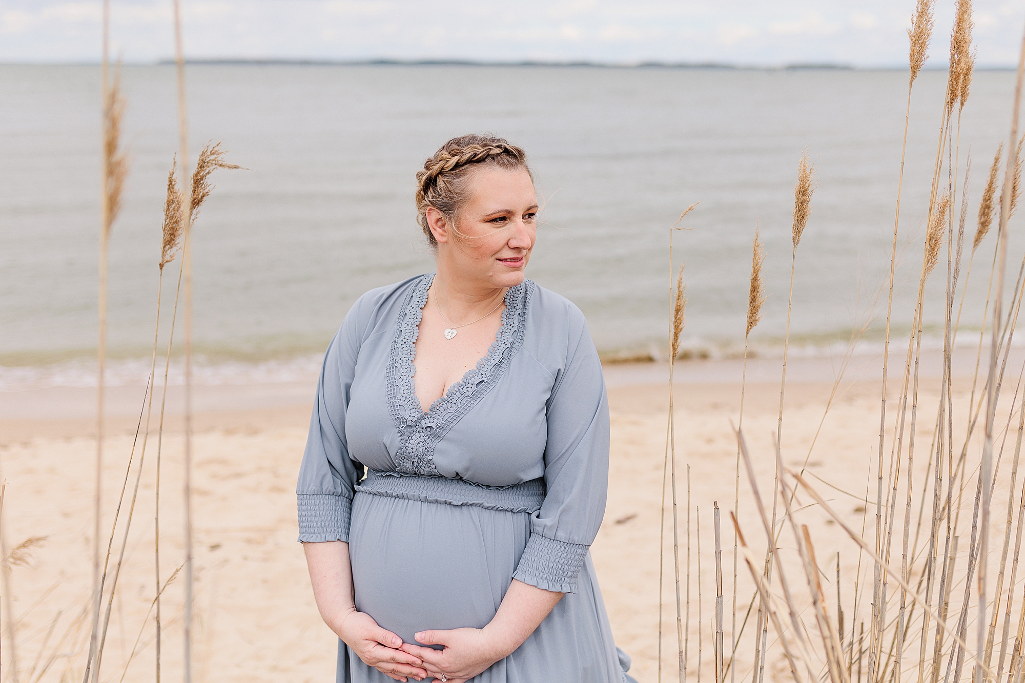 mom holds belly during MD maternity photos on the beach 