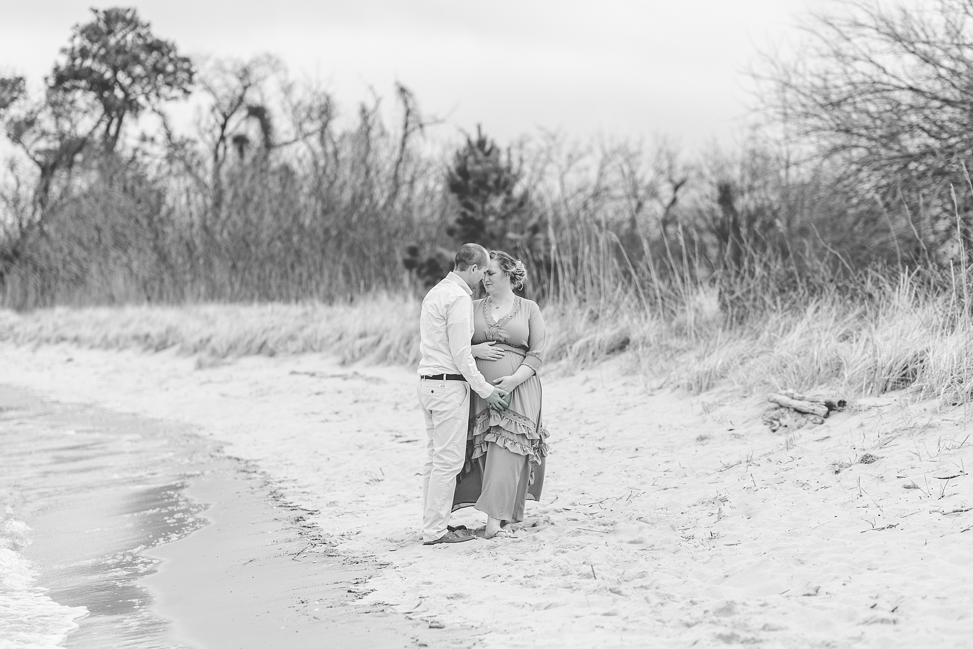couple stands together in sand during Eastern Shore maternity portraits