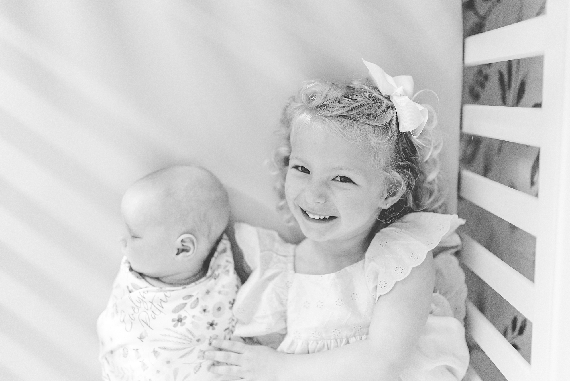 sister lays with newborn sister in crib during Maryland lifestyle newborn session