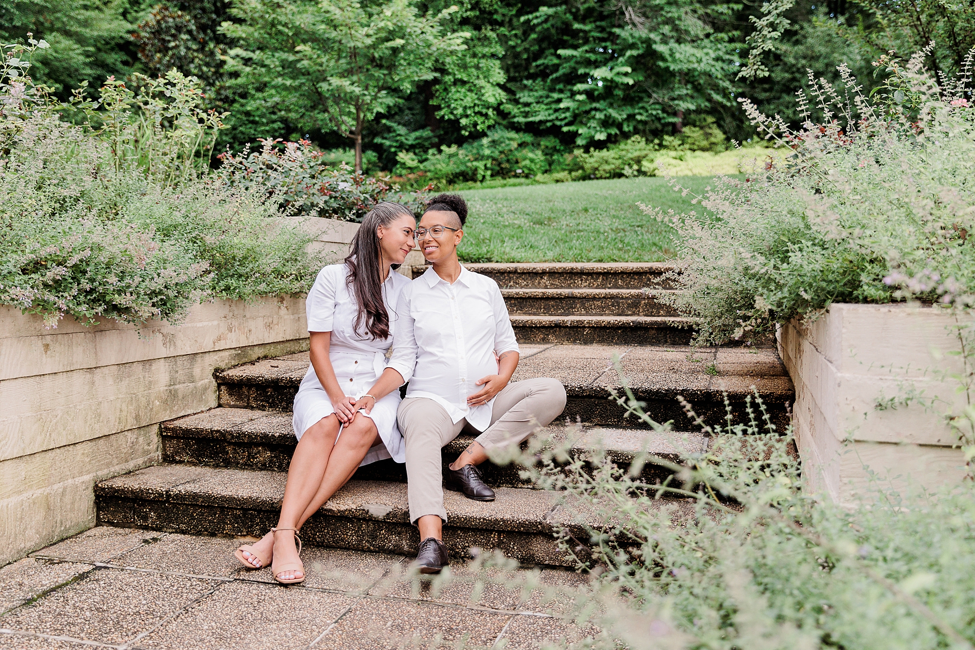women sit on steps in Bethesda garden during maternity session