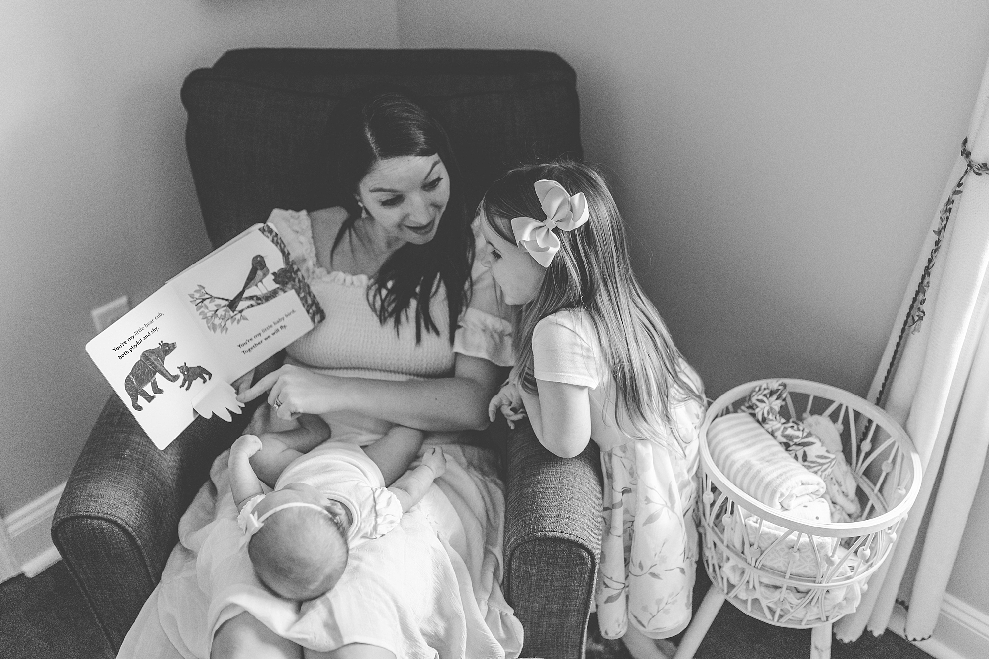 mom sits in nursery chair with new baby girl and big sister 