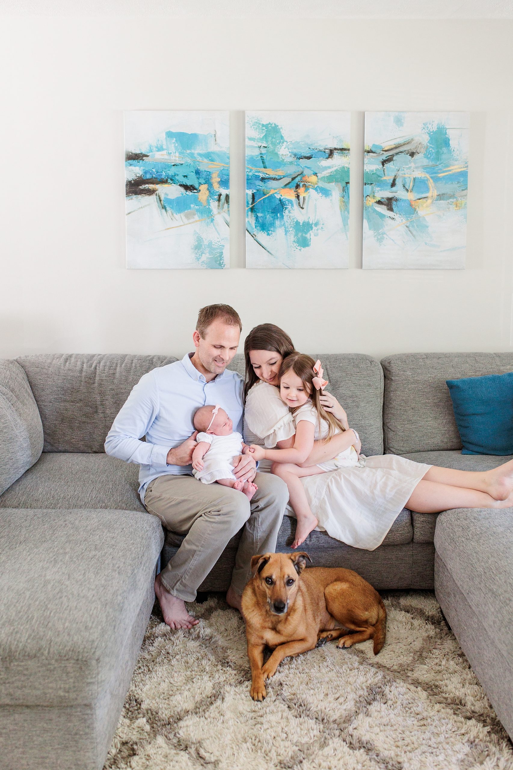 family sits on couch with new baby and dog at their feet during Annapolis MD lifestyle newborn session