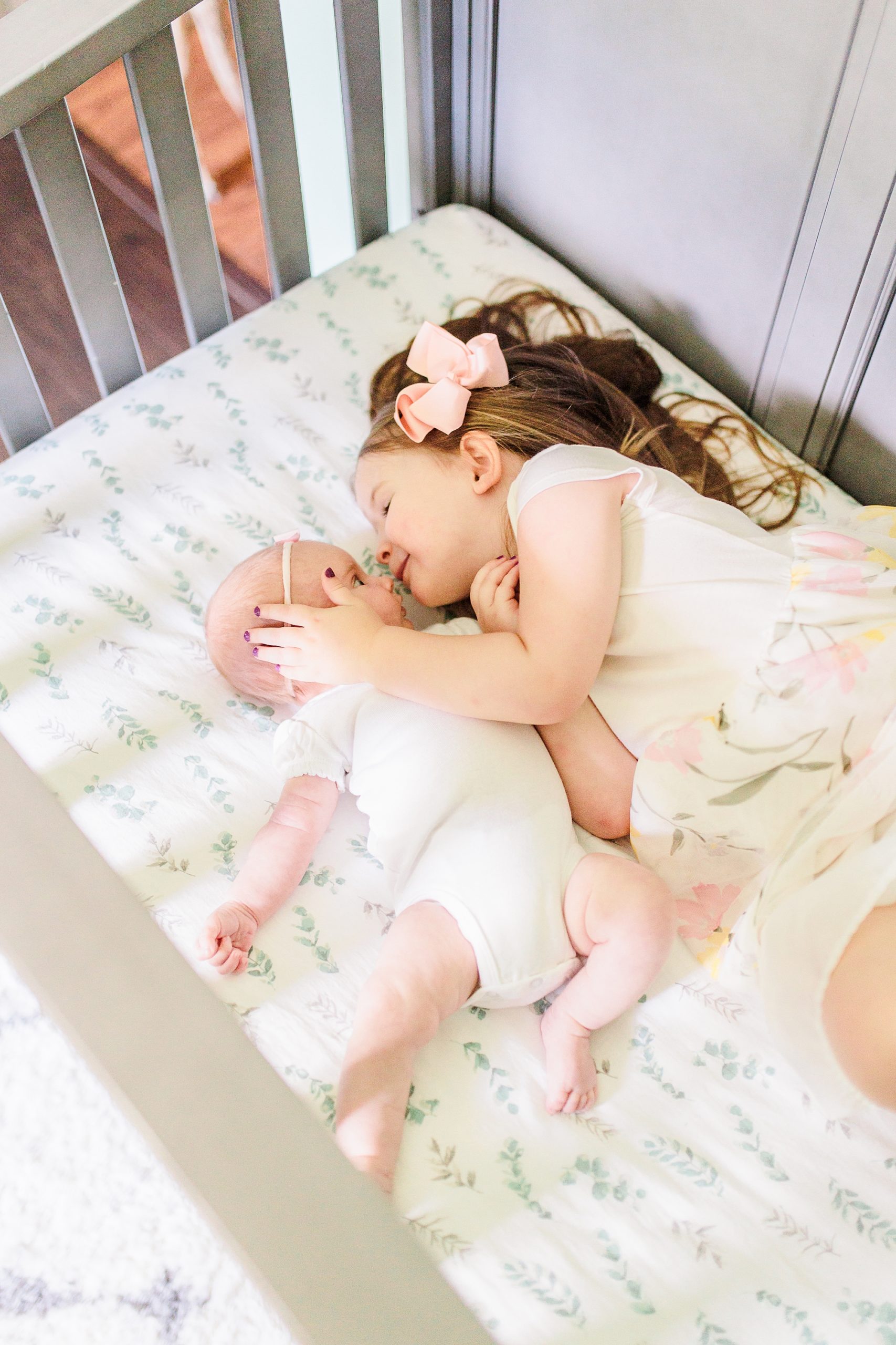 big sister kisses little sister's nose laying in crib