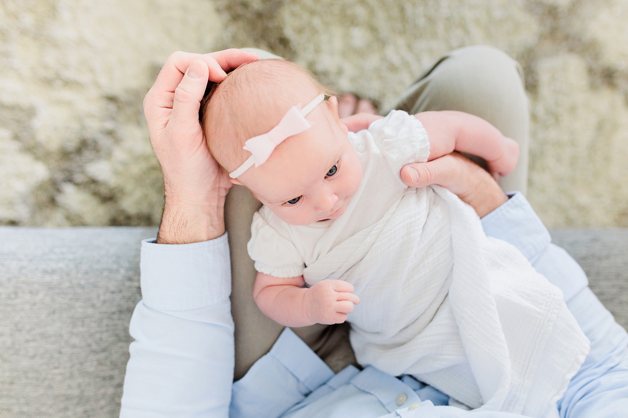dad holds daughter in white onesie with white bow