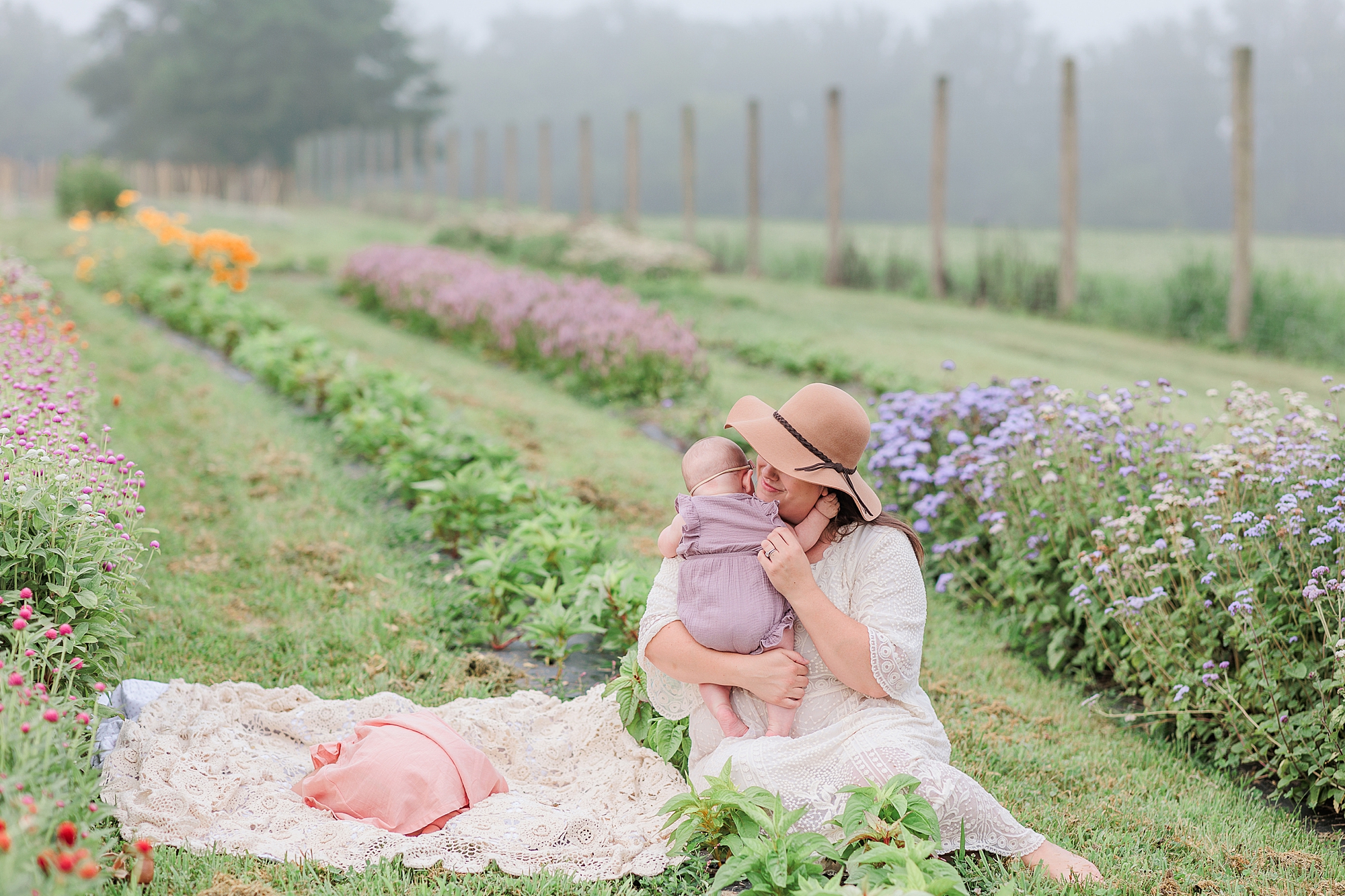 mom holds baby while sister lays on blanket in field of wildflowers 