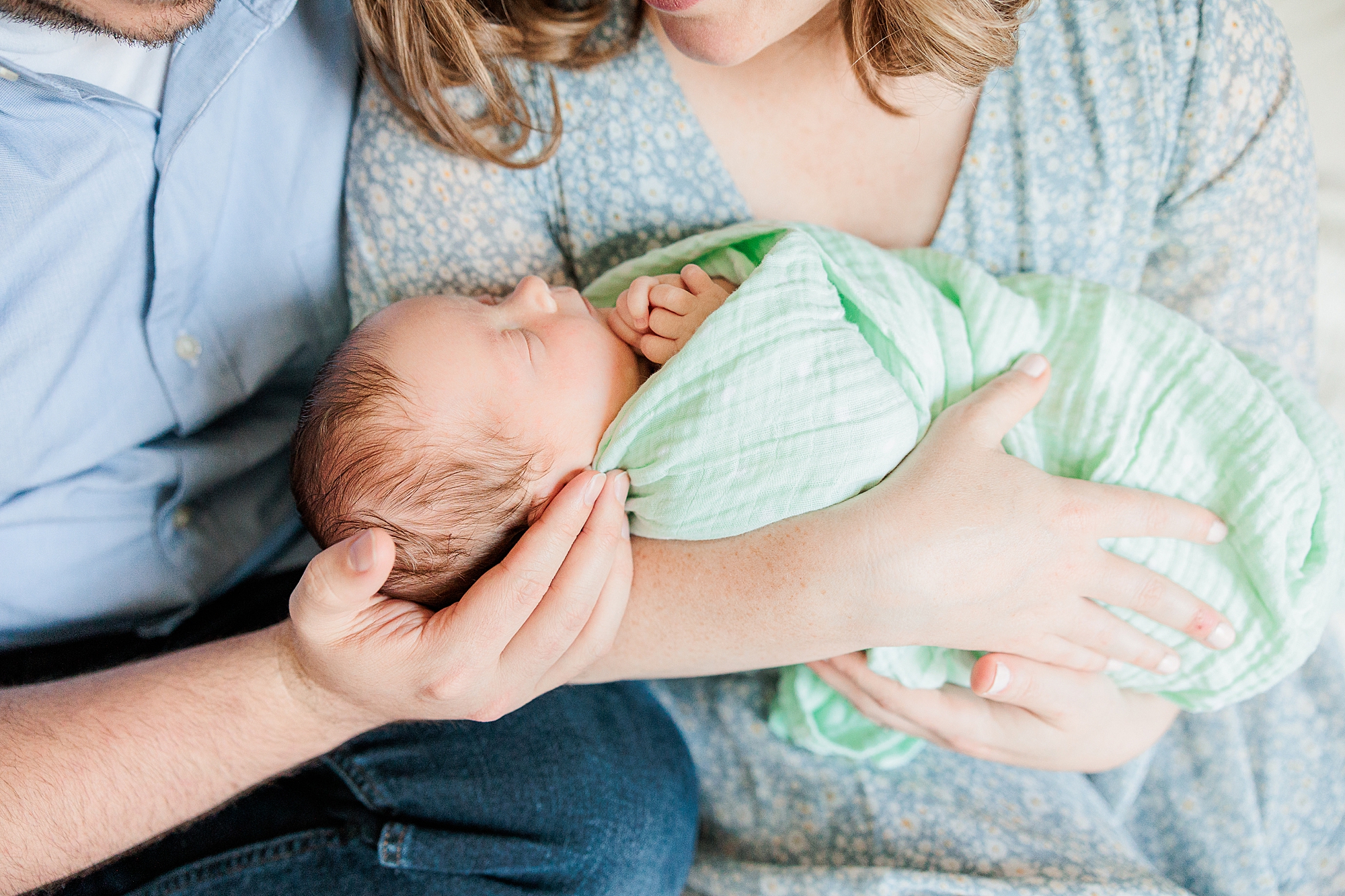 parents snuggle baby girl in green wrap during lifestyle newborn session