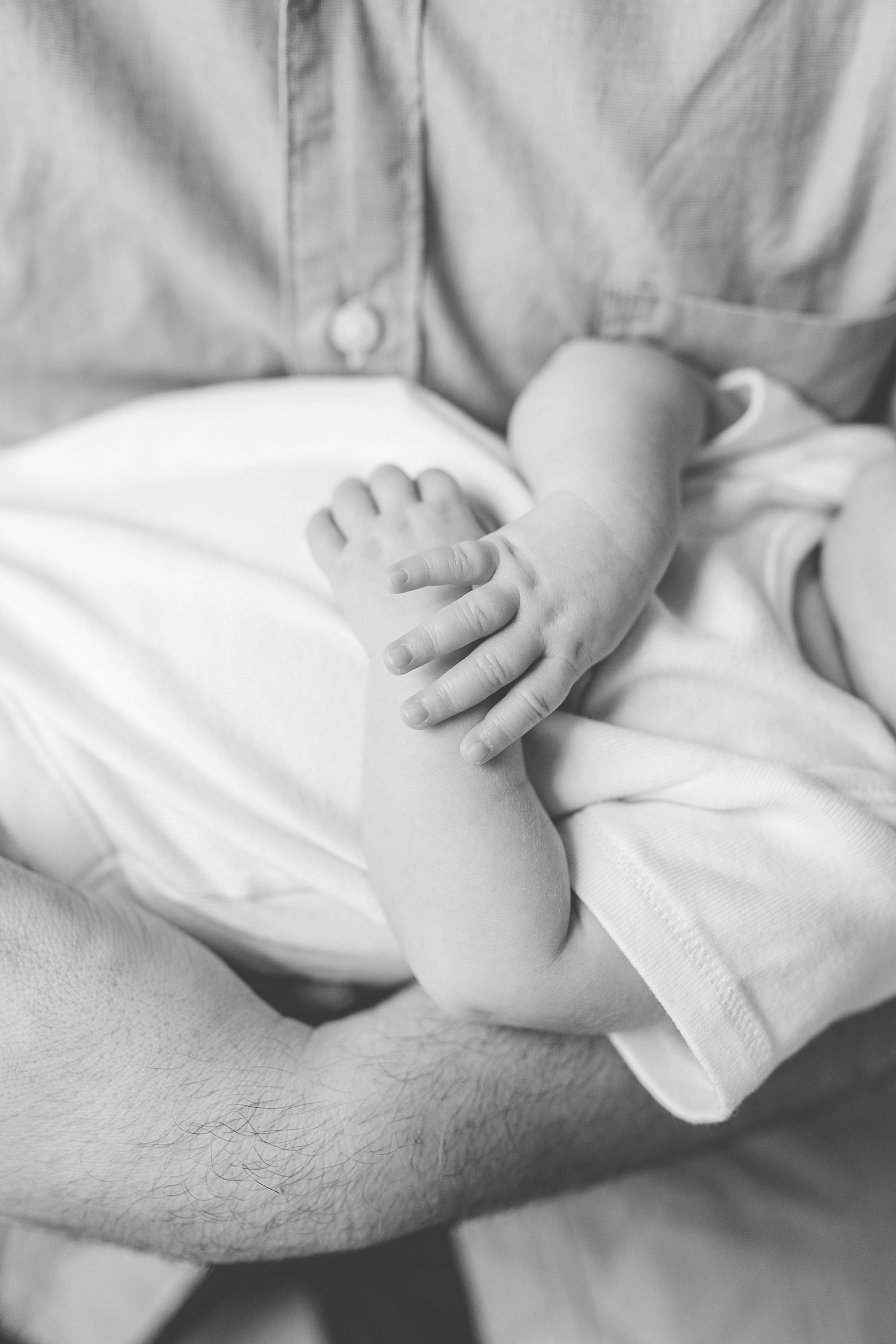 baby holds hands laying on dad's arms