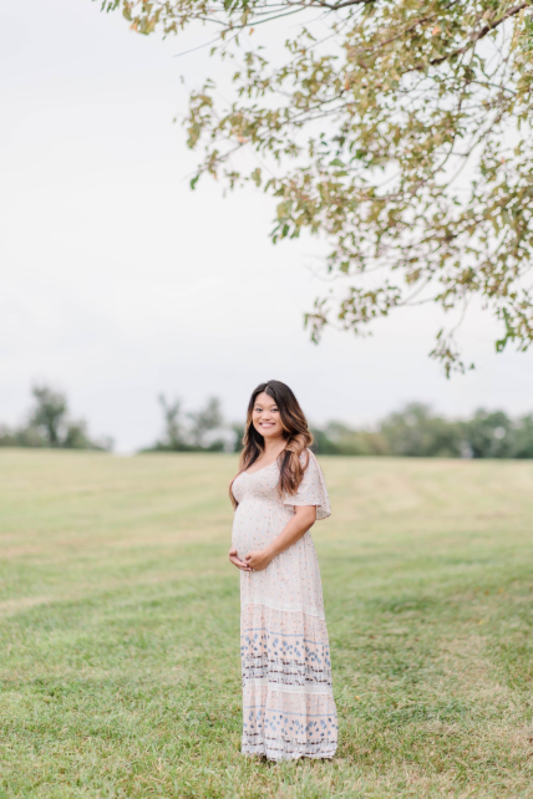 mother stands in field holding baby bump