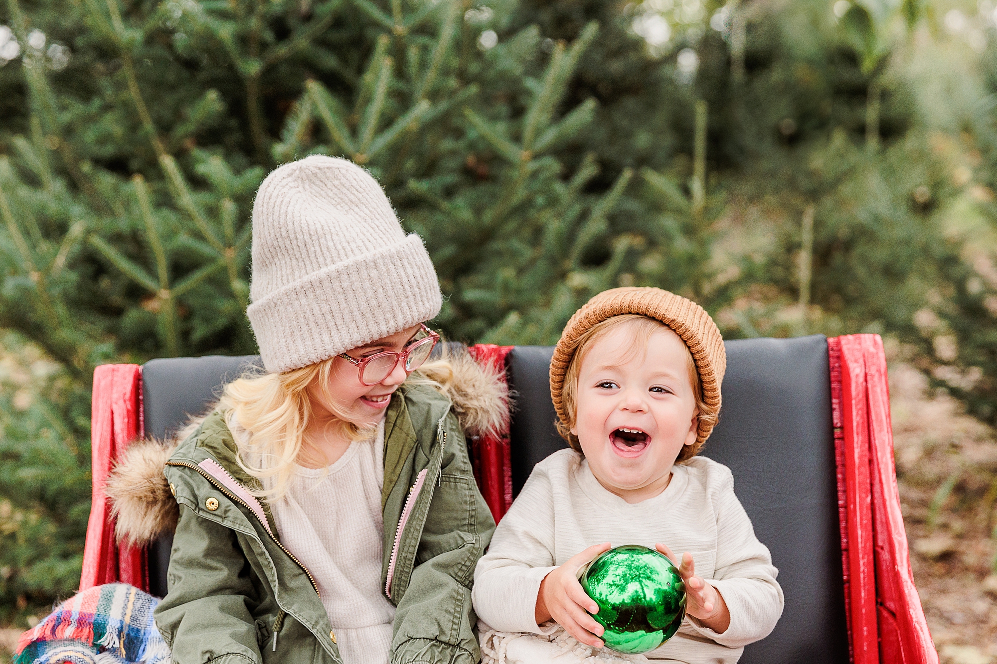 toddler laughs holding green ornament during Maryland family portraits on Christmas tree farm